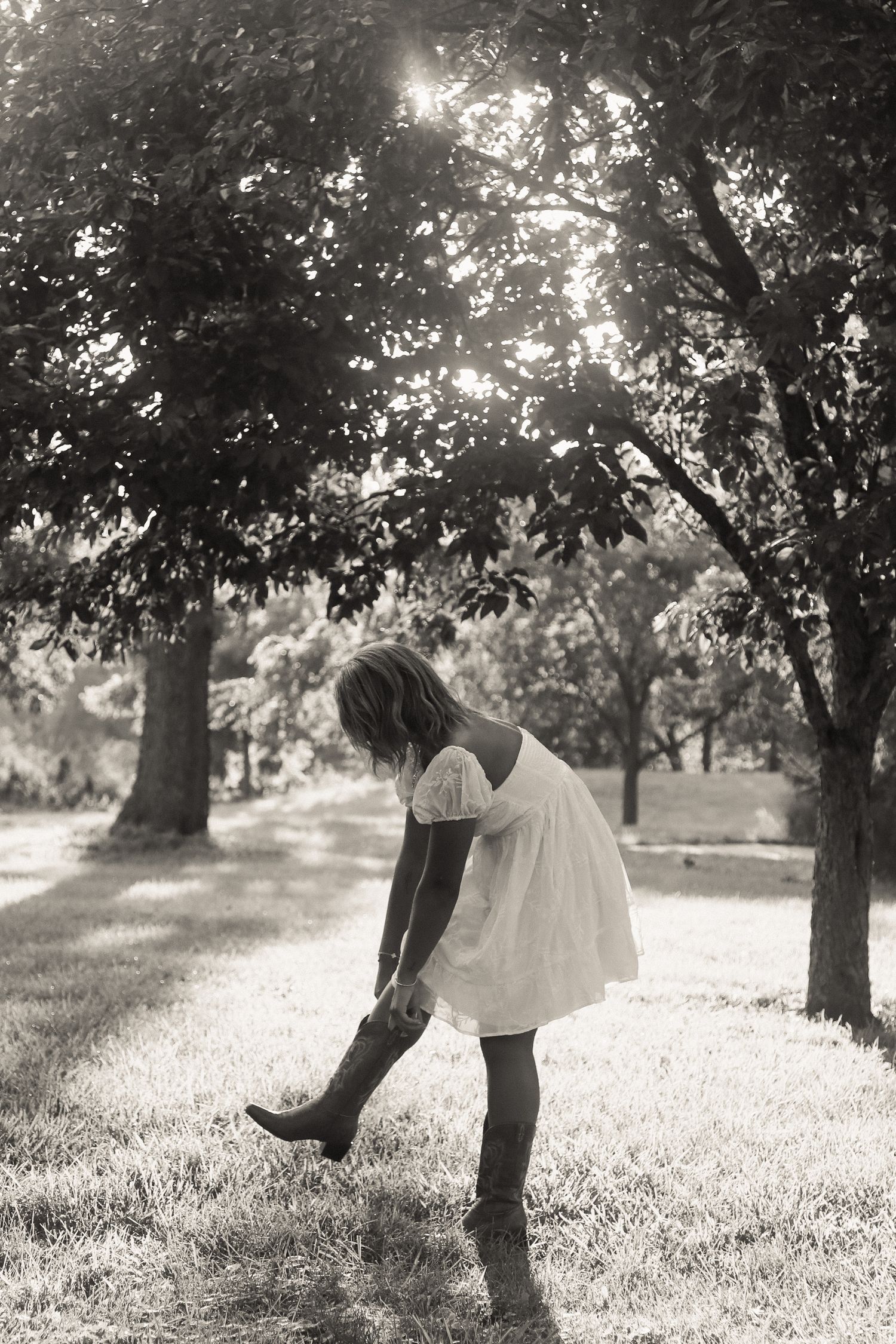 Artistic black and white photo of someone playfully posing among trees in a grassy field.