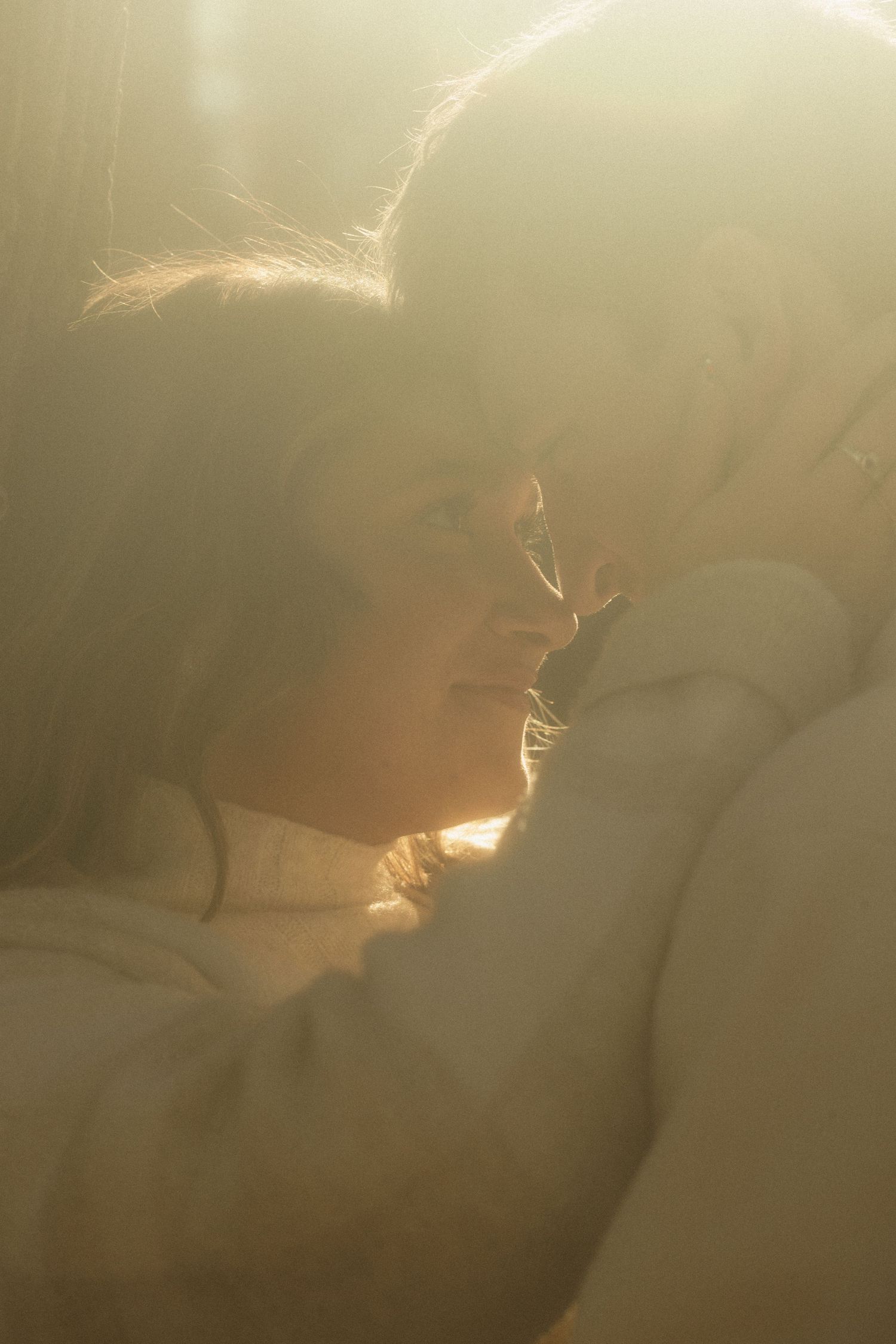 A dreamy backlit close-up portrait of a couple sharing an intimate moment in soft golden light.