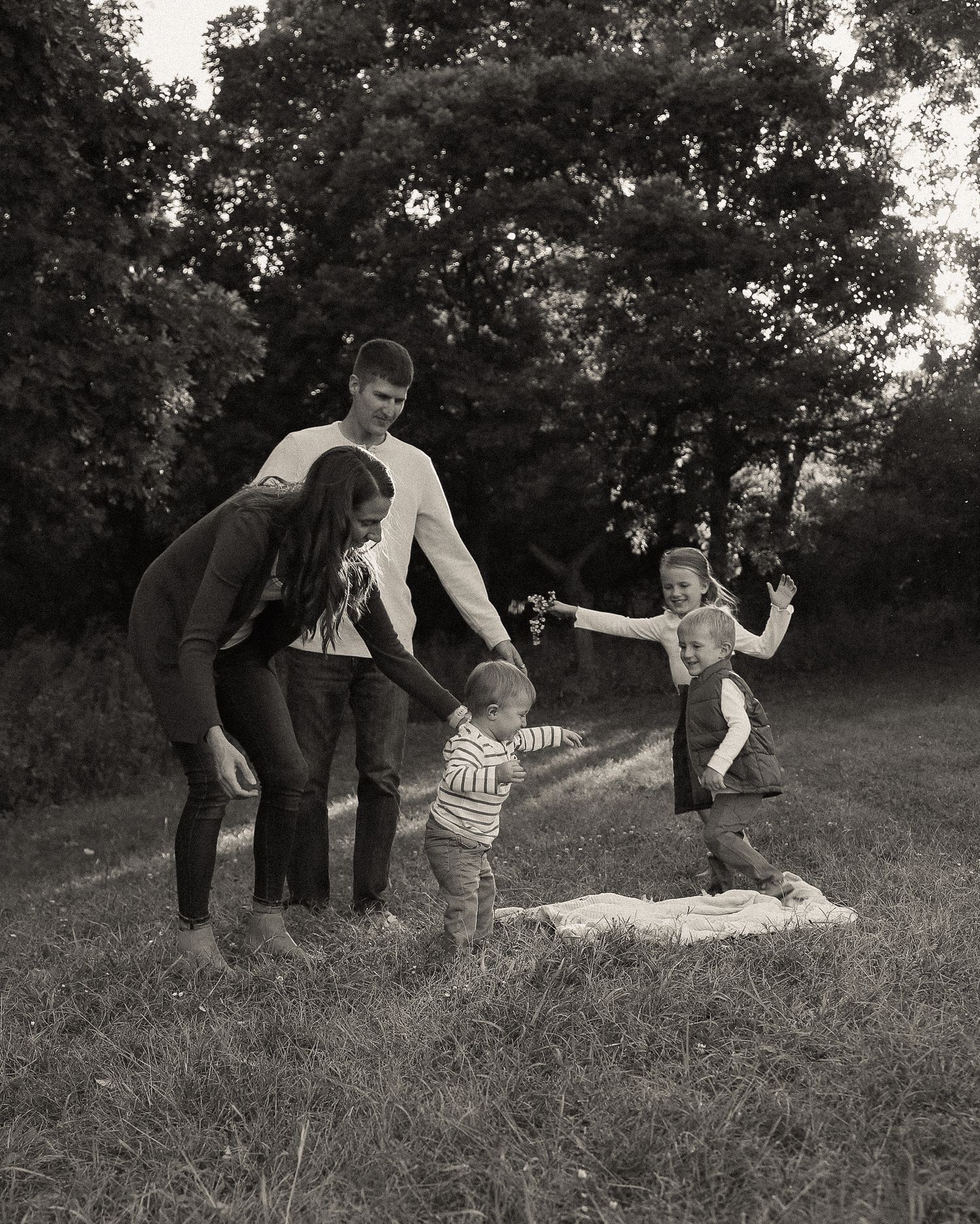 Family enjoying playful moments together on grassy hillside in black and white.