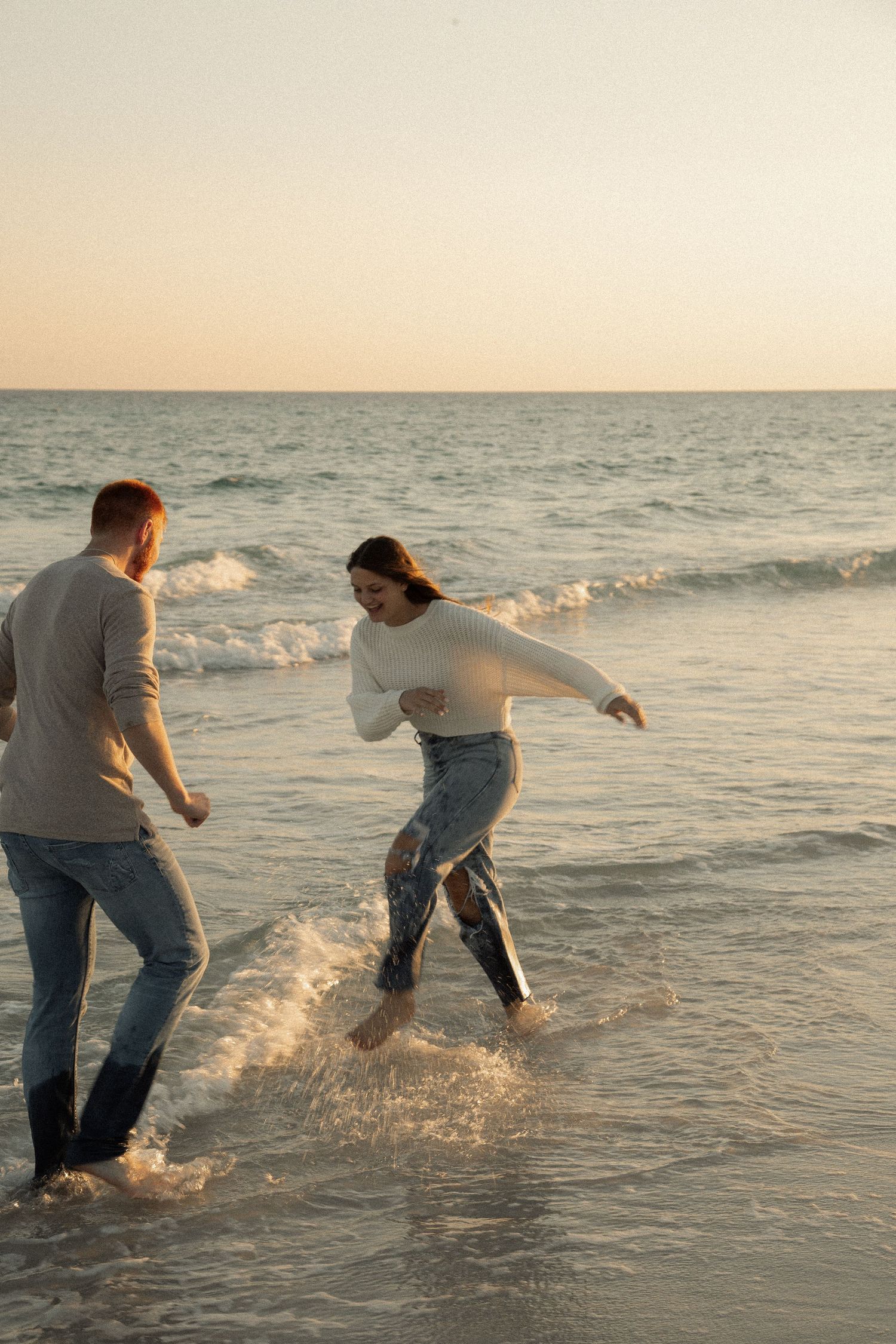 Couple playfully splashing and running through ocean waves at sunset.