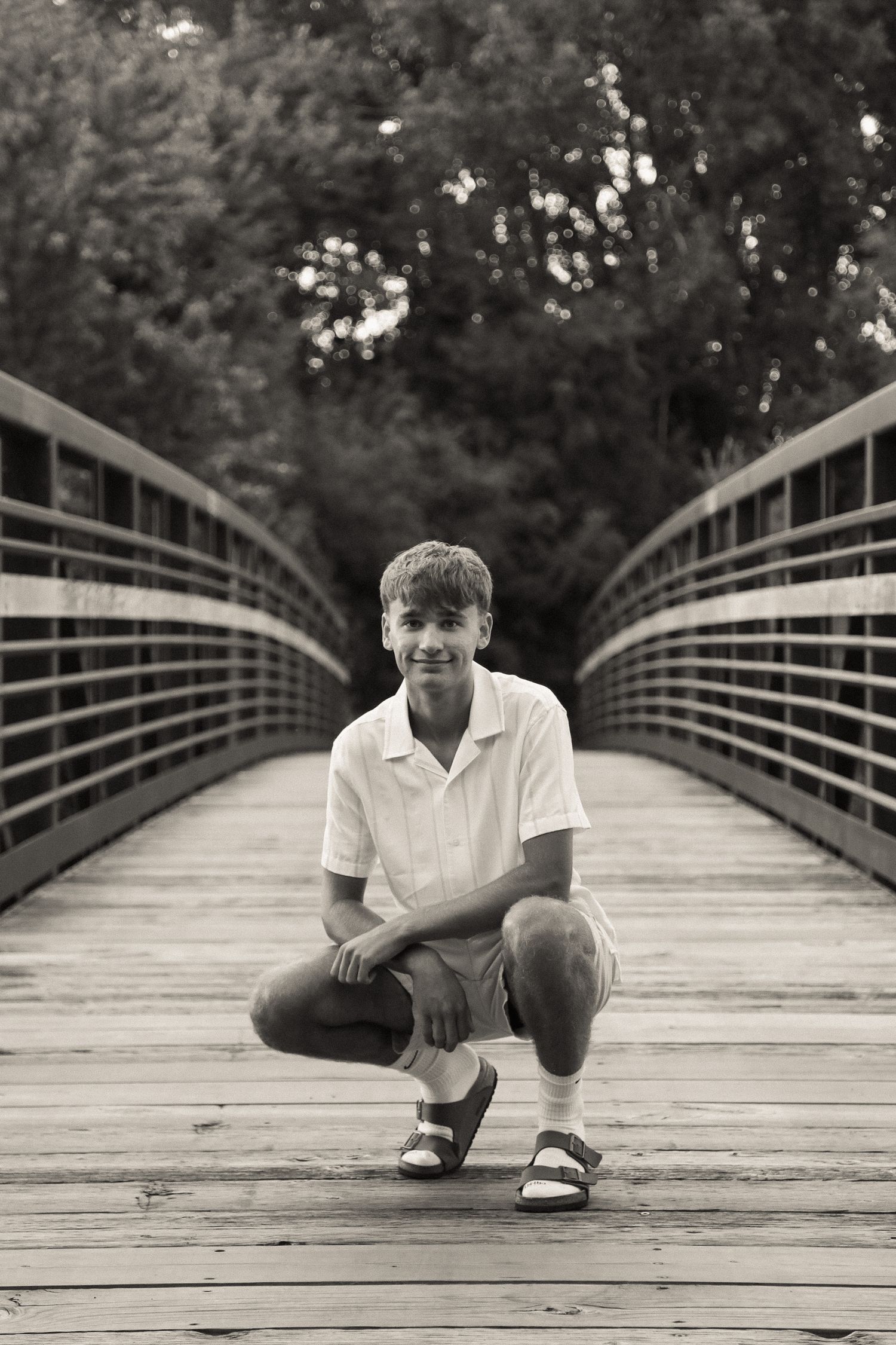Black and white photo of someone sitting on a wooden bridge deck in casual attire.