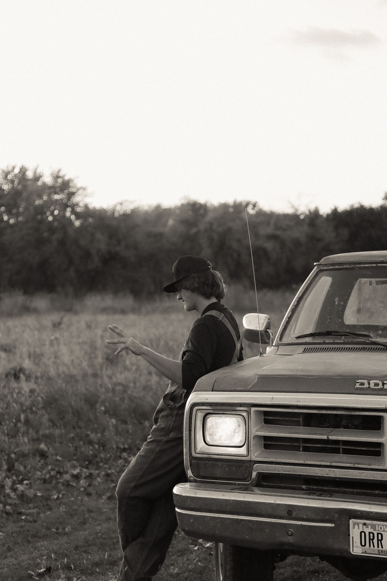 Silhouette of someone standing beside classic Dodge truck in evening light.