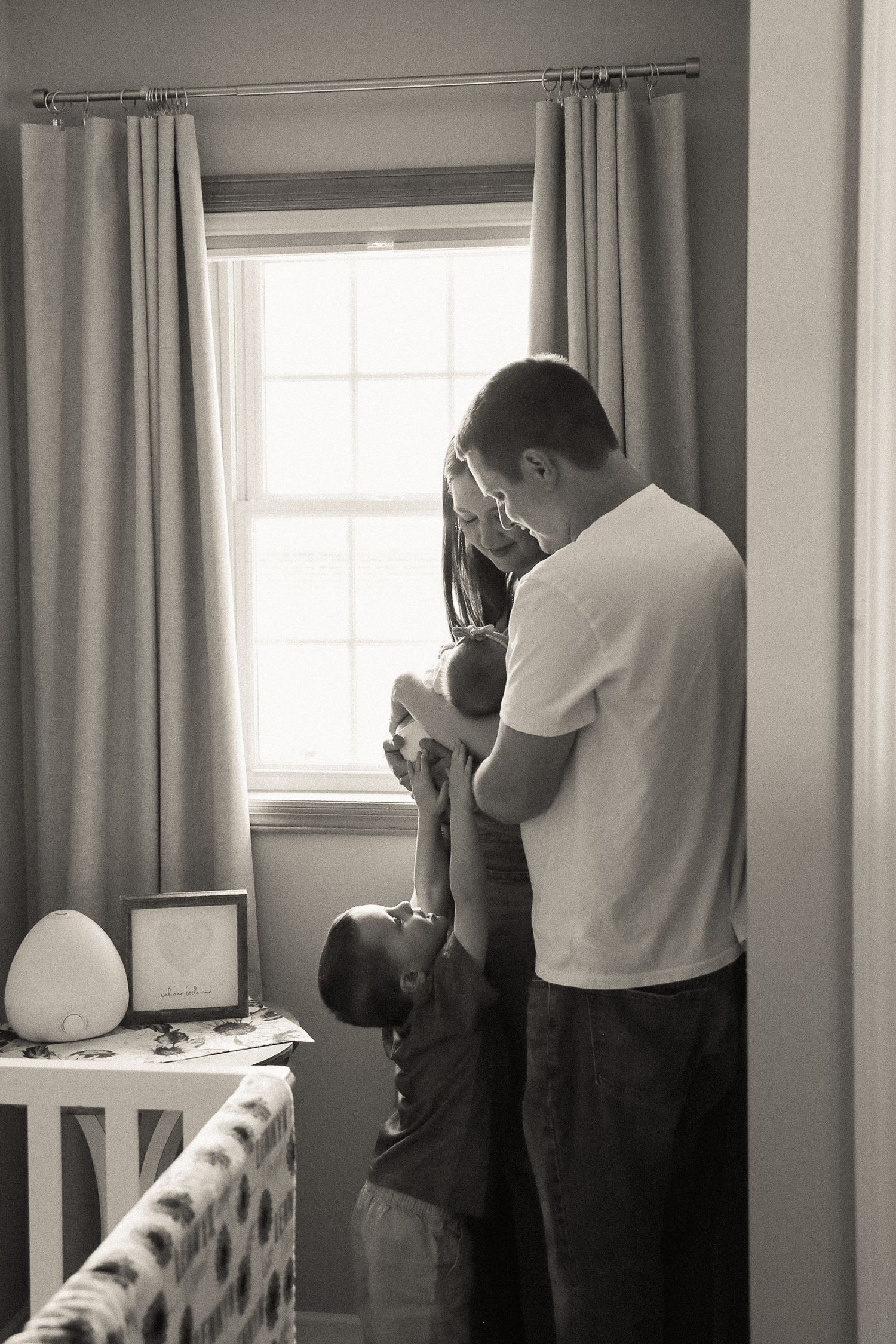 A couple stands together in a room with grey curtains and natural window light.