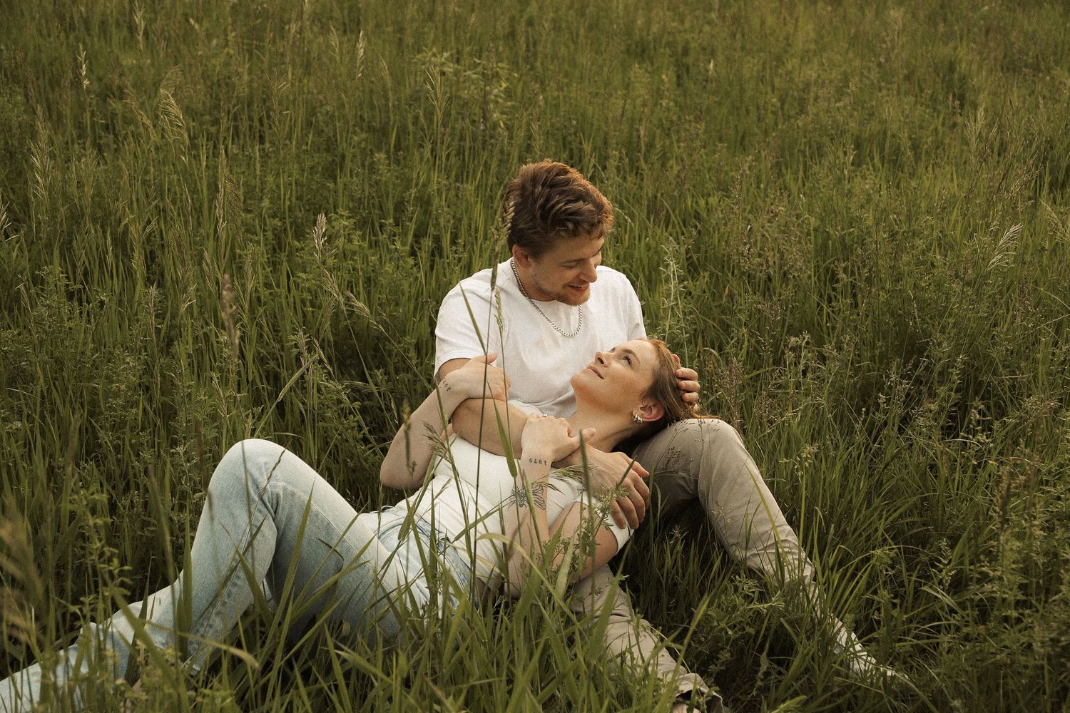 A couple embracing in a field of tall grass during sunset.