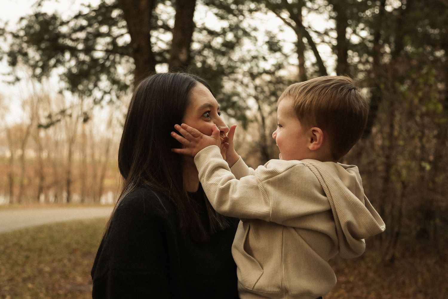 A toddler and adult share a tender outdoor moment in warm autumn lighting.