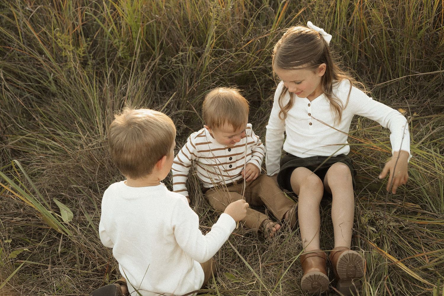 Playful family moment captured in tall grass during outdoor photoshoot.