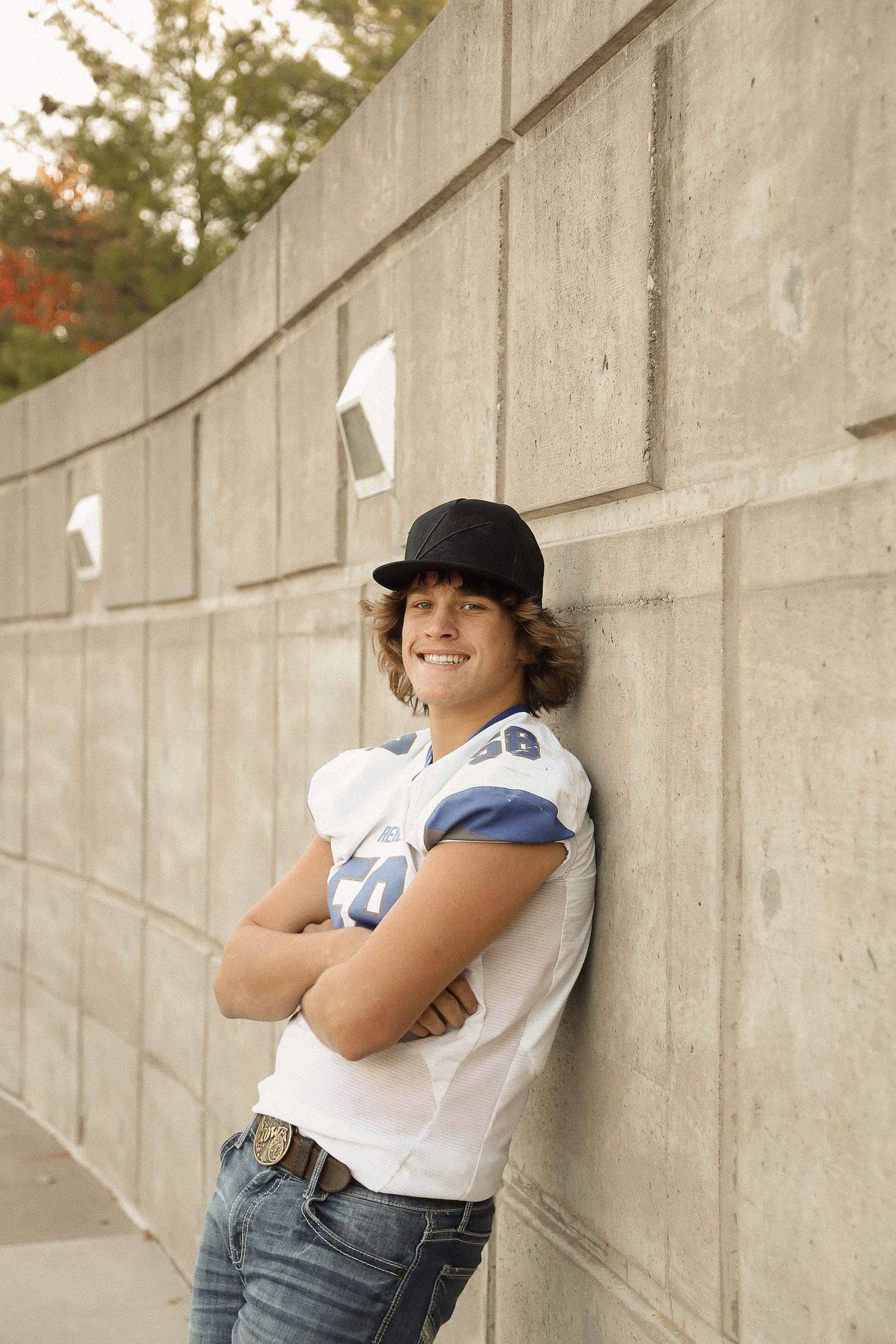Person in a baseball cap and white t-shirt poses playfully against a curved concrete wall.