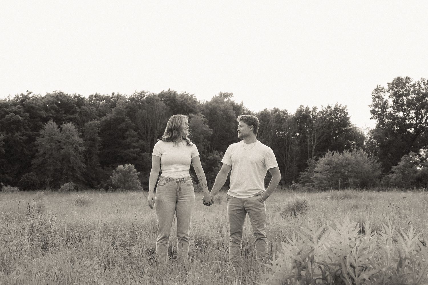 A couple walking hand in hand through a grassy field at sunset.
