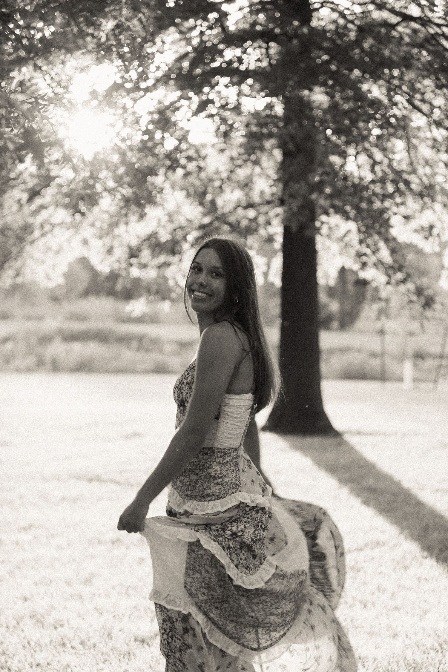 A flowy patterned dress twirls in a black and white outdoor photoshoot with trees in the background.