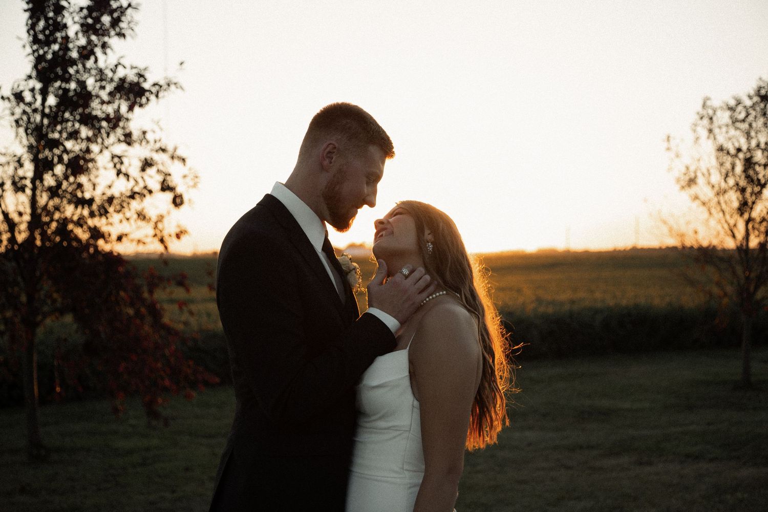 A tender moment between newlyweds backlit by a glowing sunset in an outdoor setting.