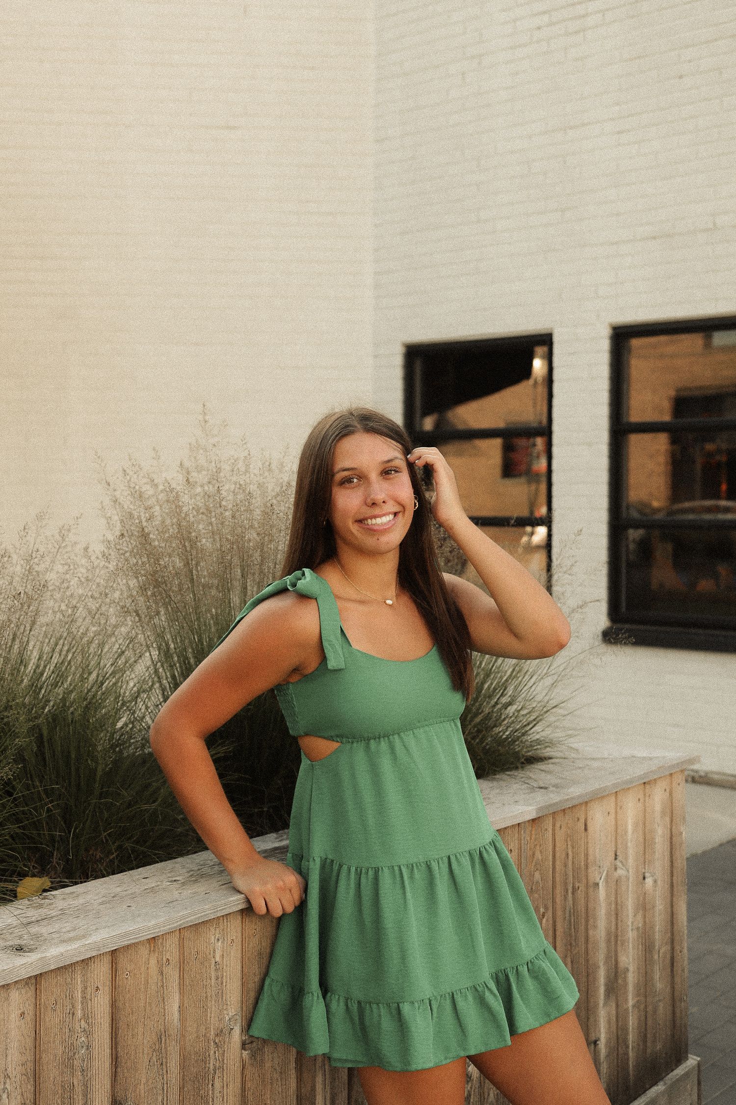 Person in green tiered summer dress posing casually against wooden fence and modern building exterior.