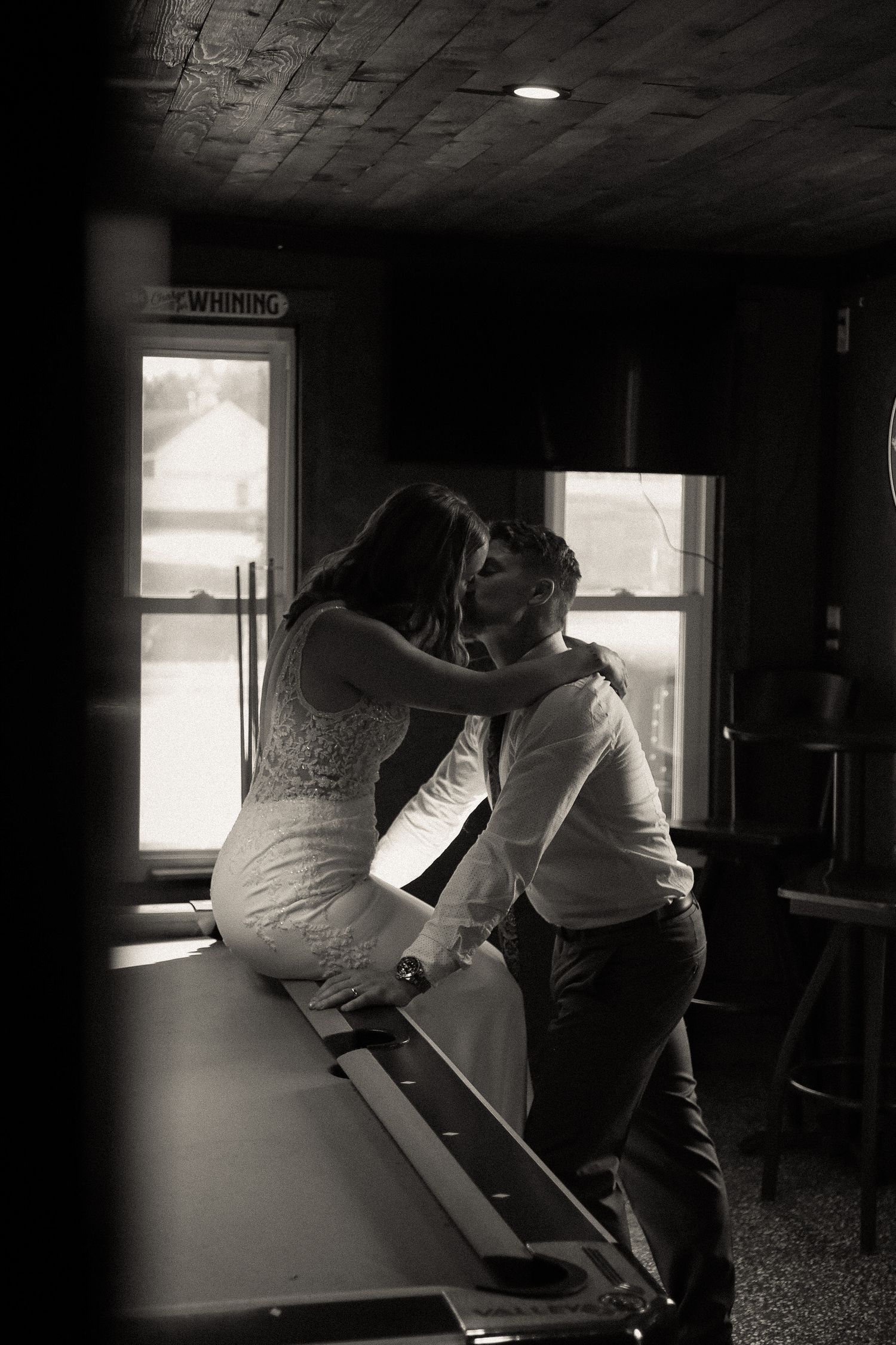 Couple in formal attire looking out a window in a dimly lit room.