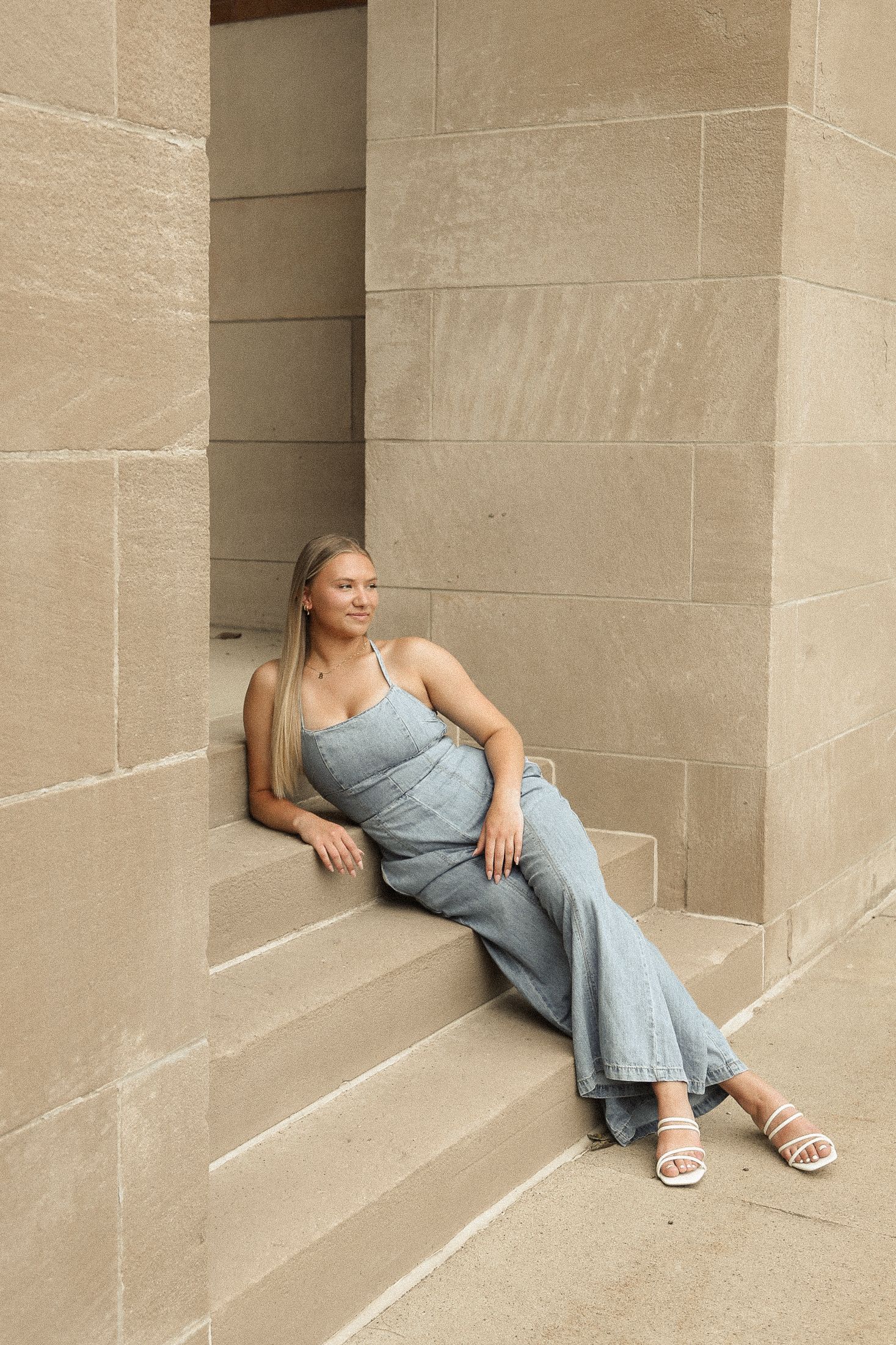 Person in a blue dress lounges casually against a stone wall in an artistic pose.