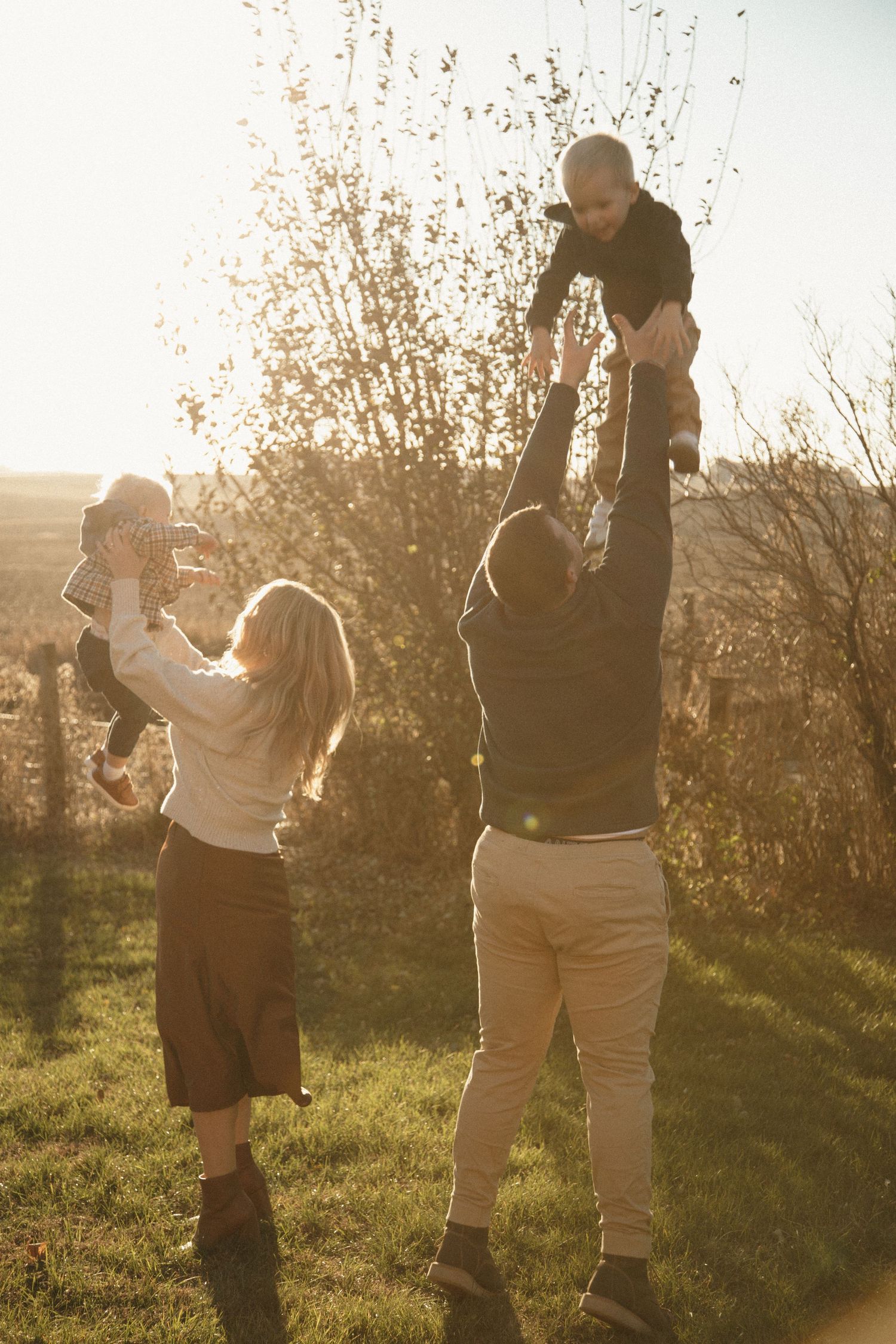 Family playing and dancing together in a sunlit field during golden hour.