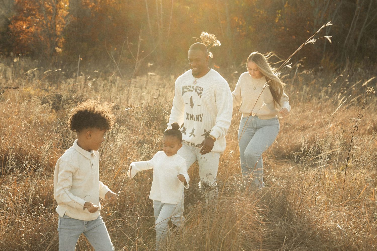 A family walks together through a golden sunlit field during autumn.