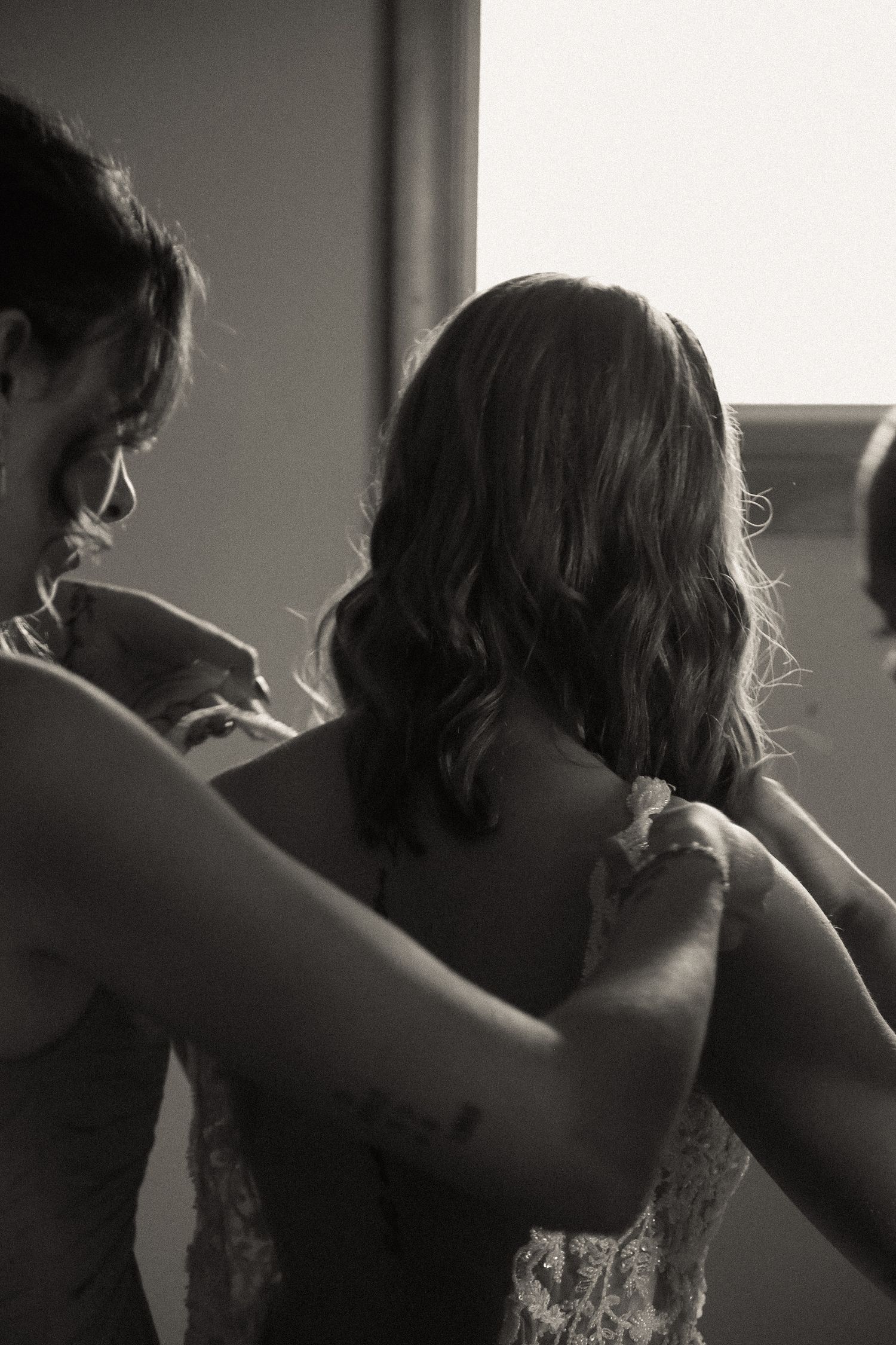 A tender moment during wedding preparations as someone helps with a dress fitting.