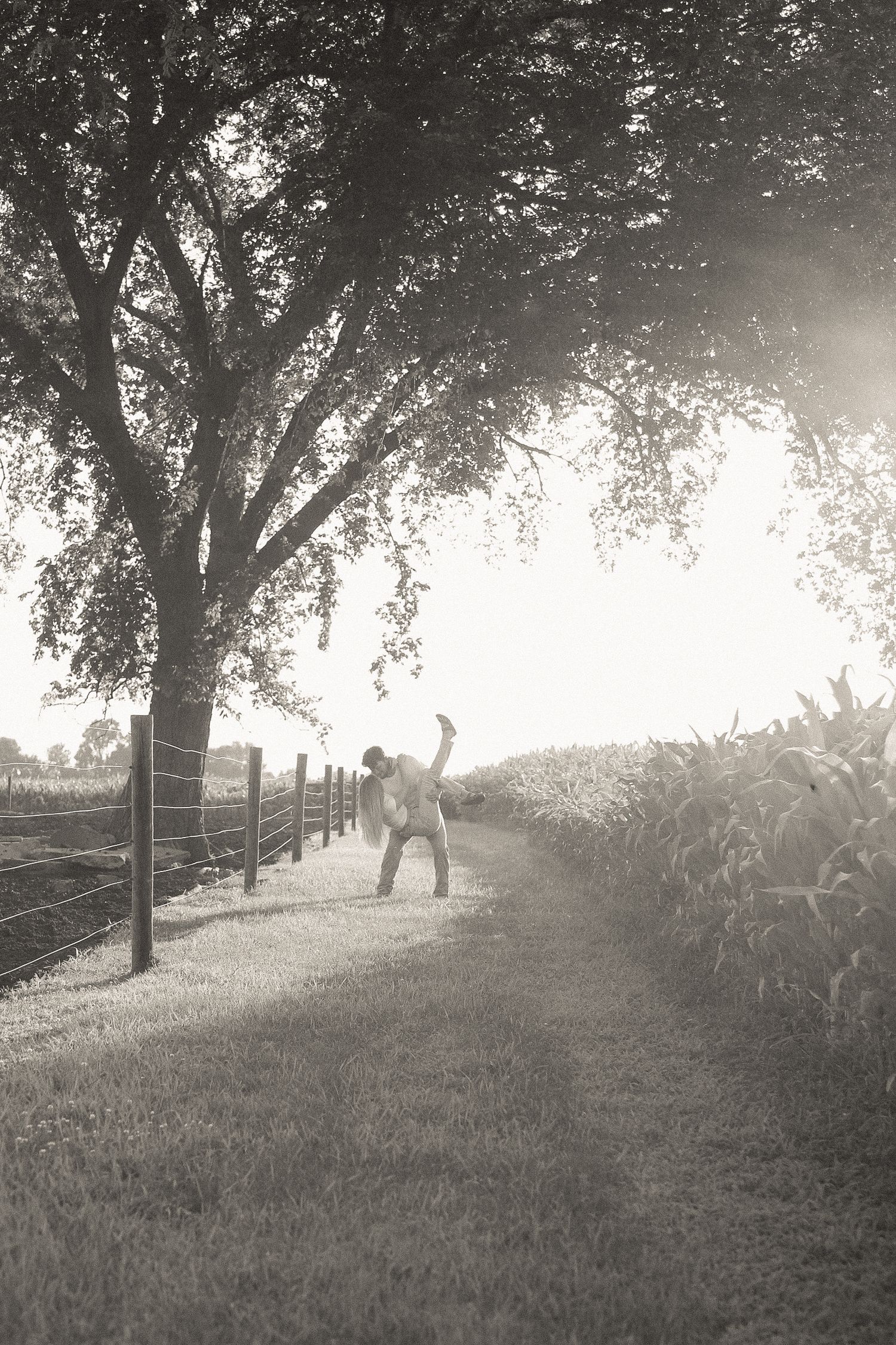 Black and white landscape photo of figures walking along a tree-lined path in misty lighting.
