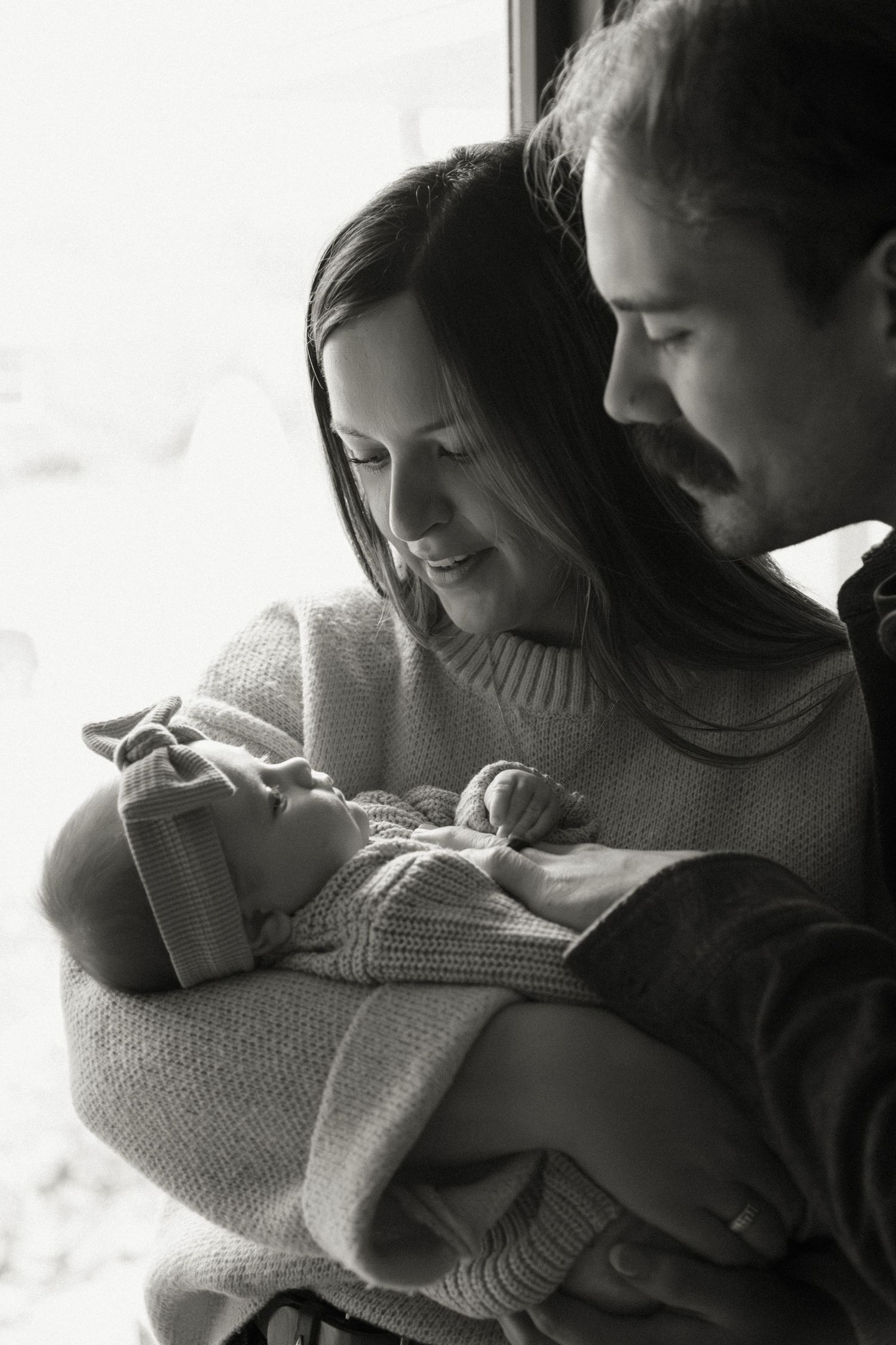 Intimate black and white family portrait showing tender moments with a newborn.