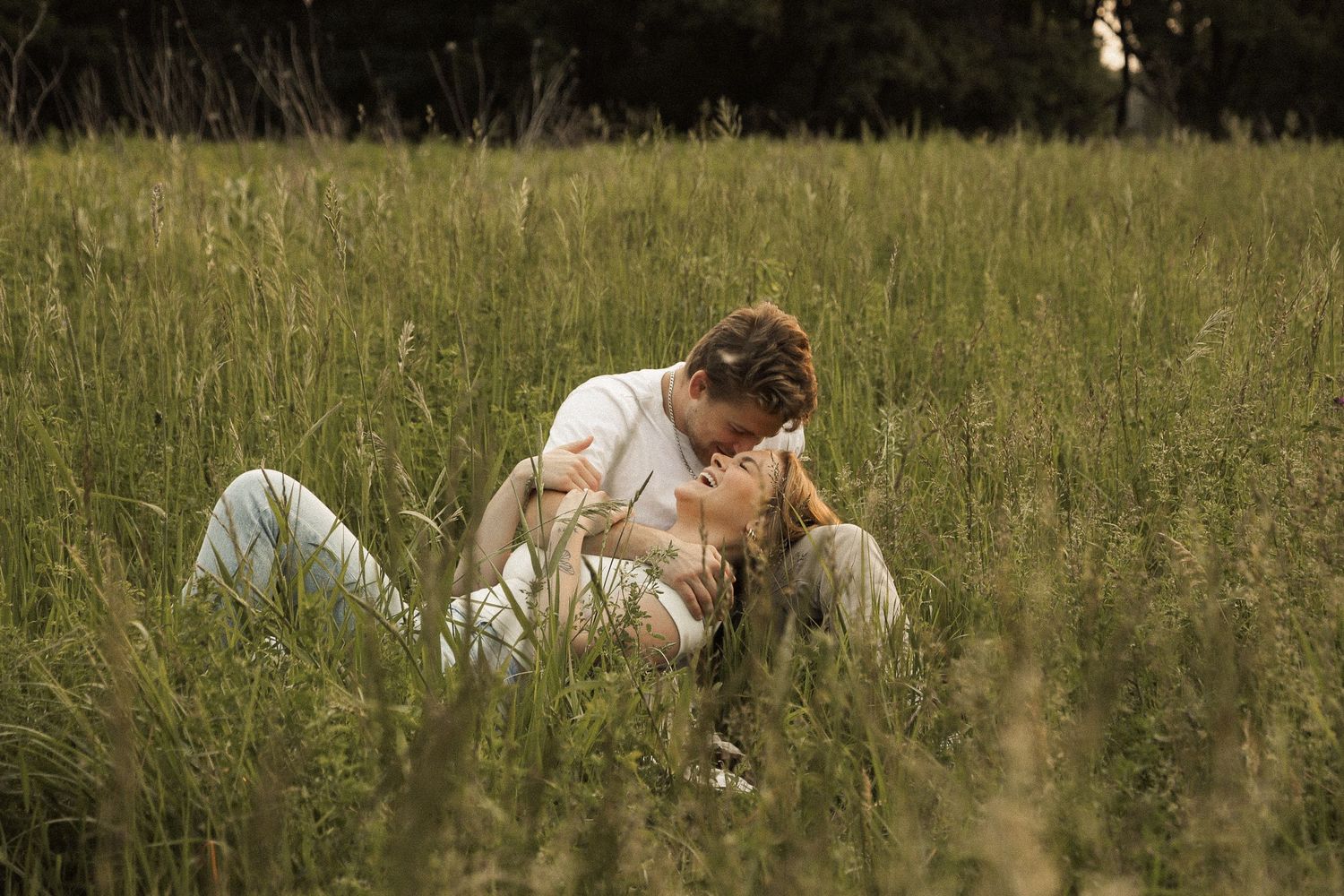 A couple sharing intimate moments in a sunlit meadow with natural greenery.