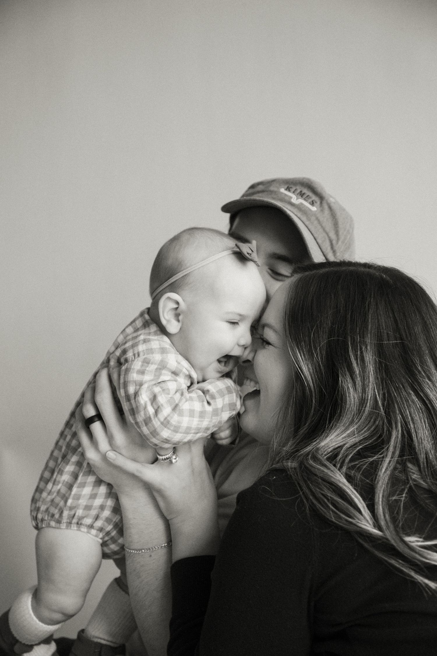 Black and white photo of happy parents kissing and cuddling their laughing baby boy.