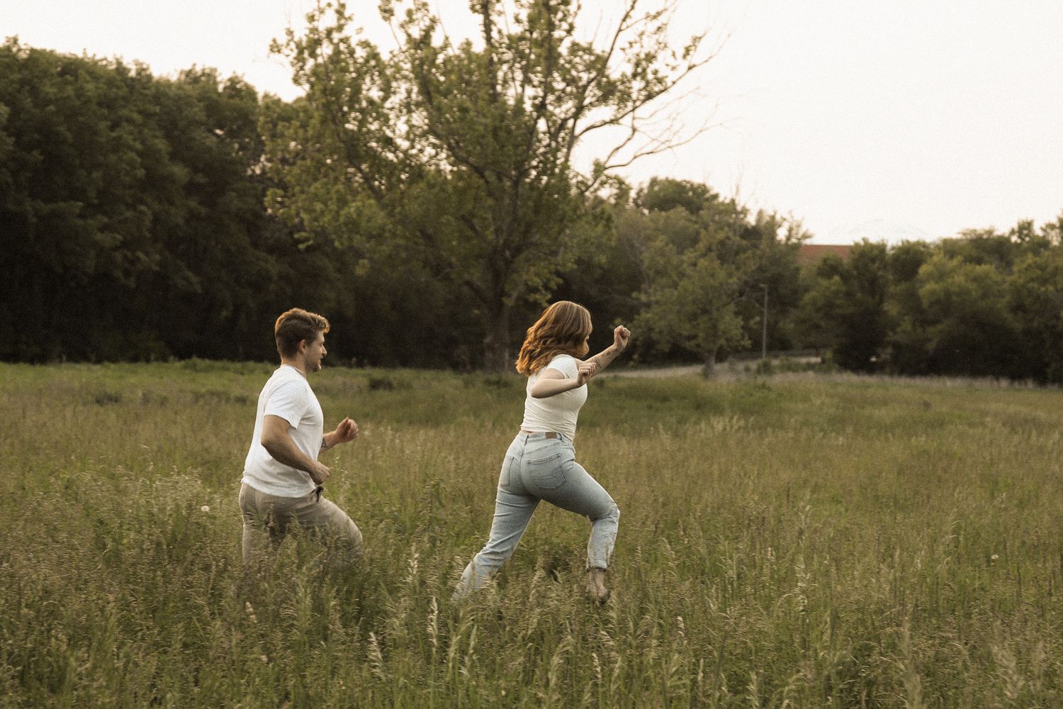 A couple playfully walking through a golden meadow at sunset.