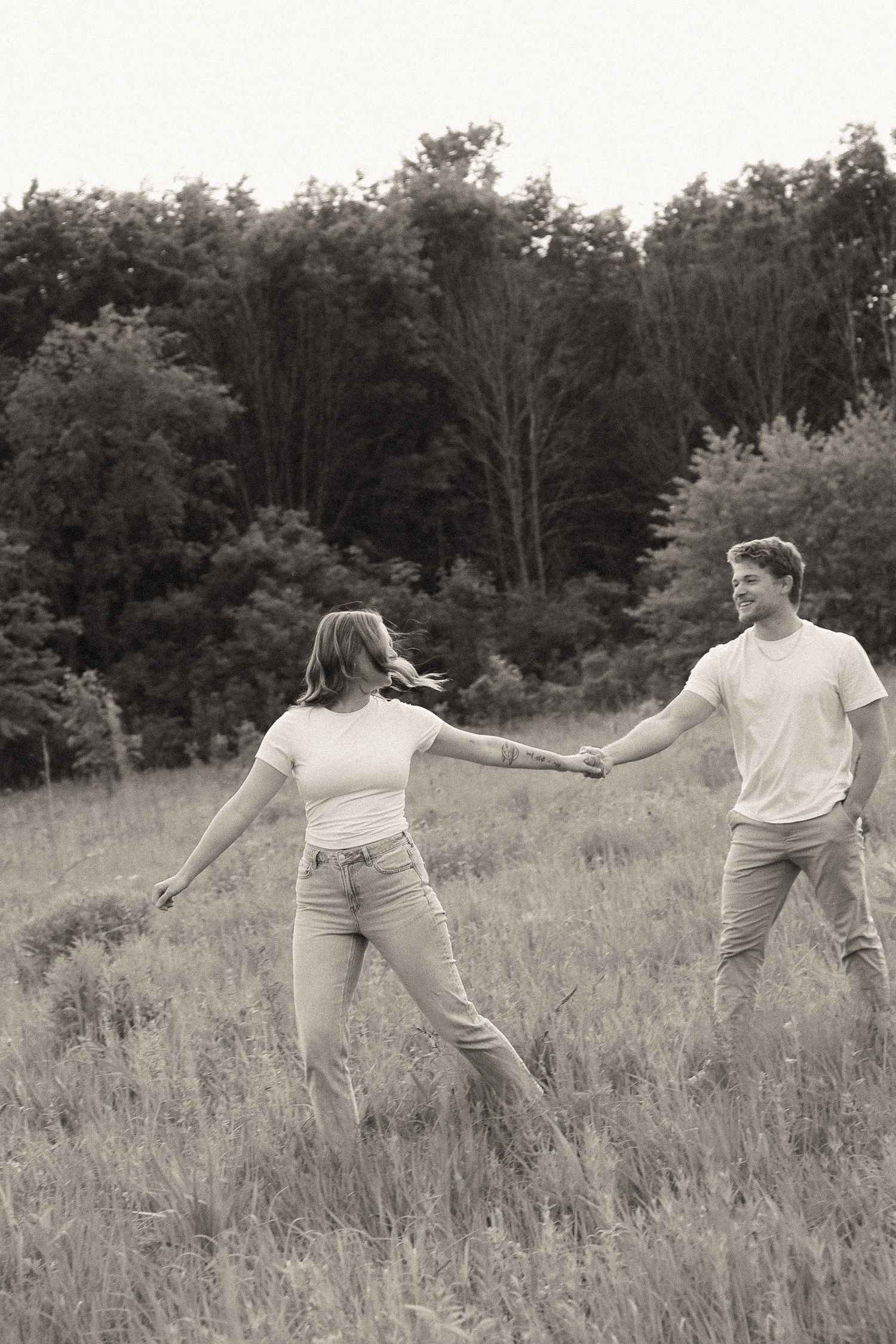 Two people dance and move expressively in a field during a black and white photo session.