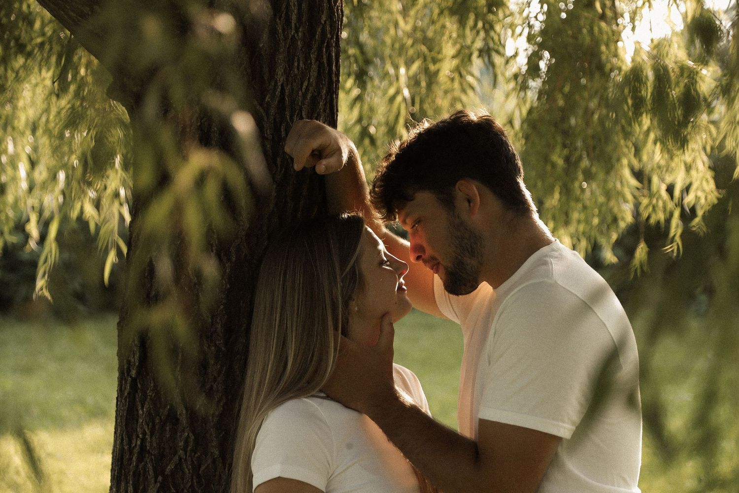Romantic couples share tender moments under willow trees in a dreamy outdoor setting.