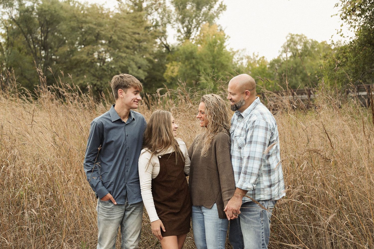 A casual family photo session captured in a natural outdoor setting with tall grass.