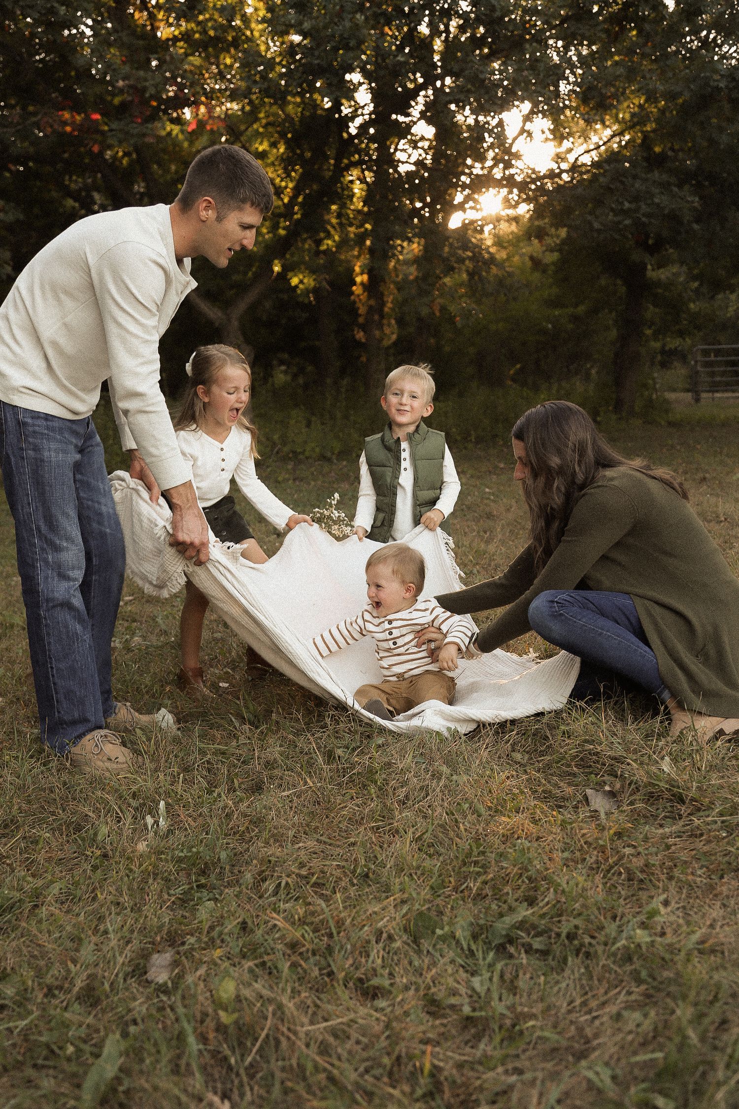 Family enjoying a tender moment together on grass during sunset with warm golden lighting.