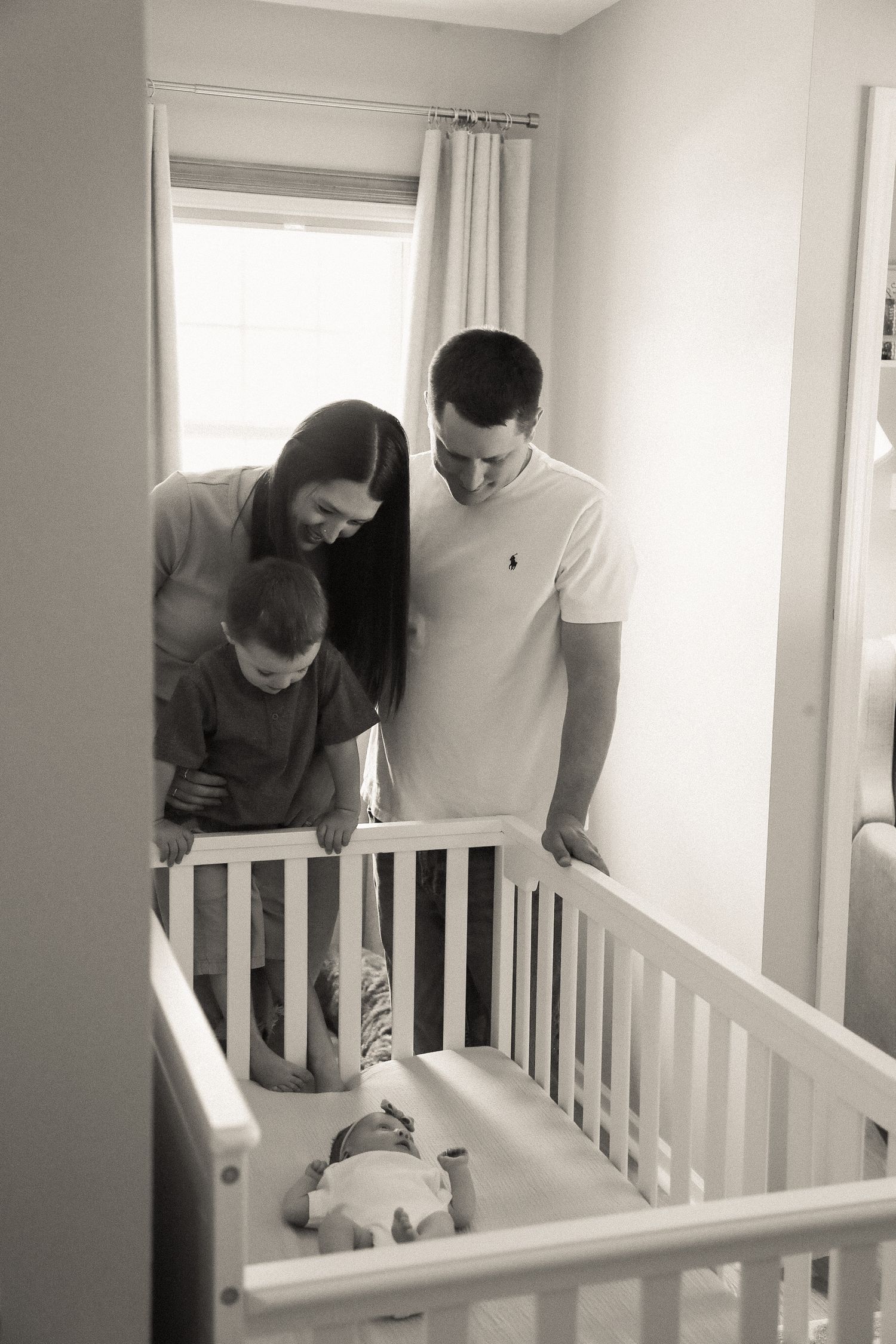 Parents lean over a white crib to tend to their baby in a bright nursery.