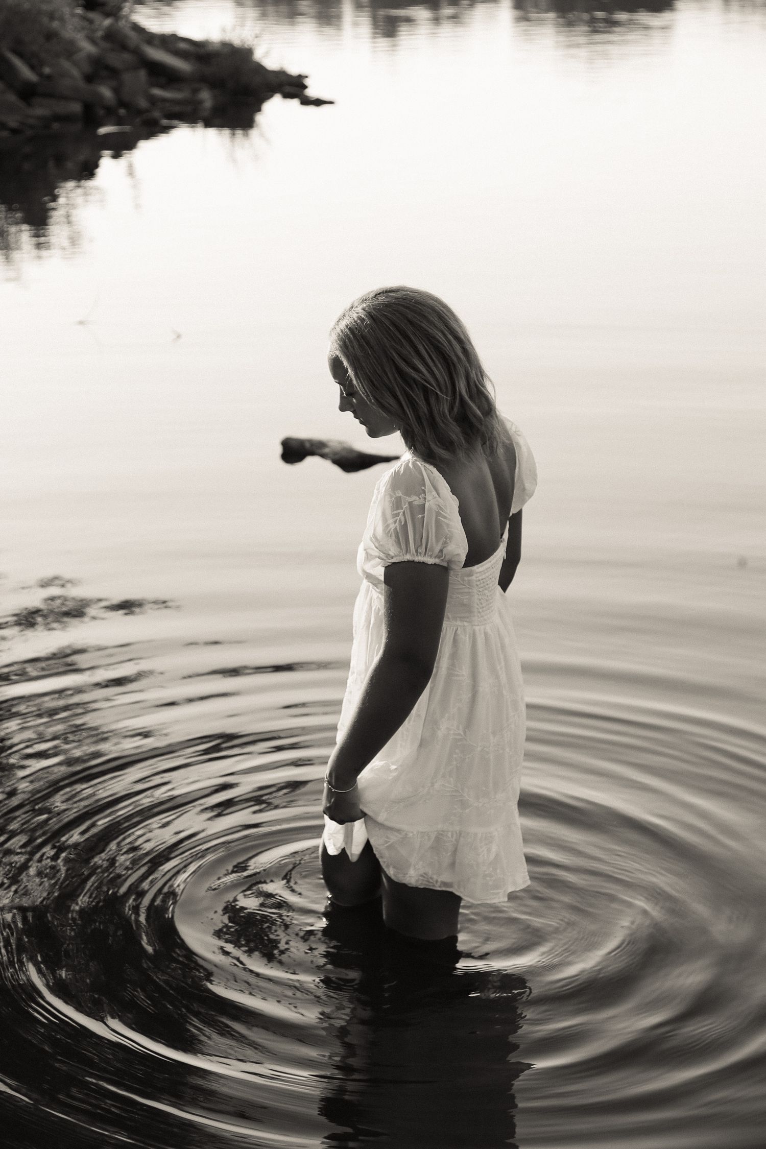Figure in white dress creates ripples while wading in still water, shown in artistic black and white sequence.