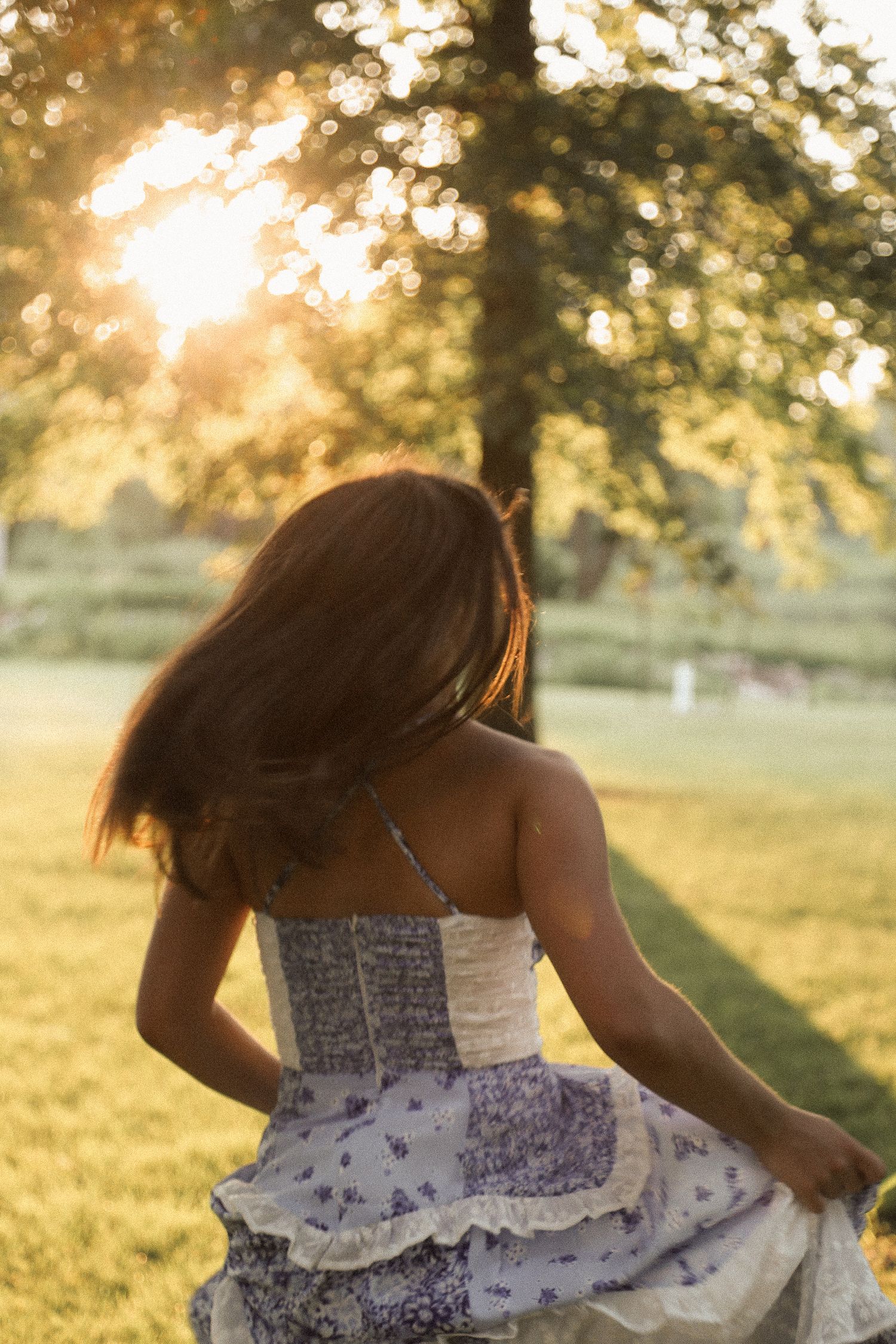 A white lace dress catches golden sunlight during a sunset photoshoot in a grassy field.