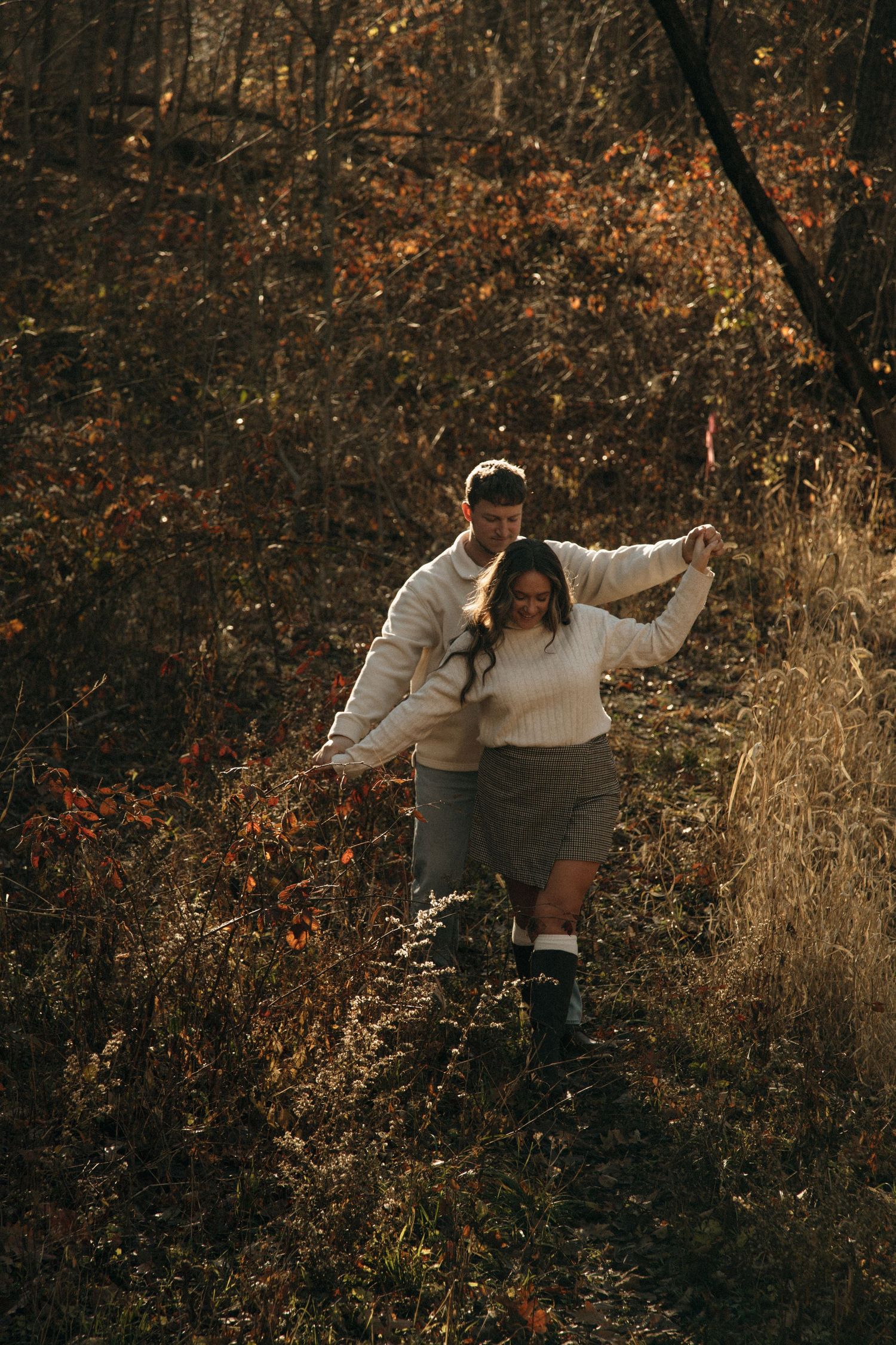 A couple dances and spins together in a golden-lit autumn forest setting.