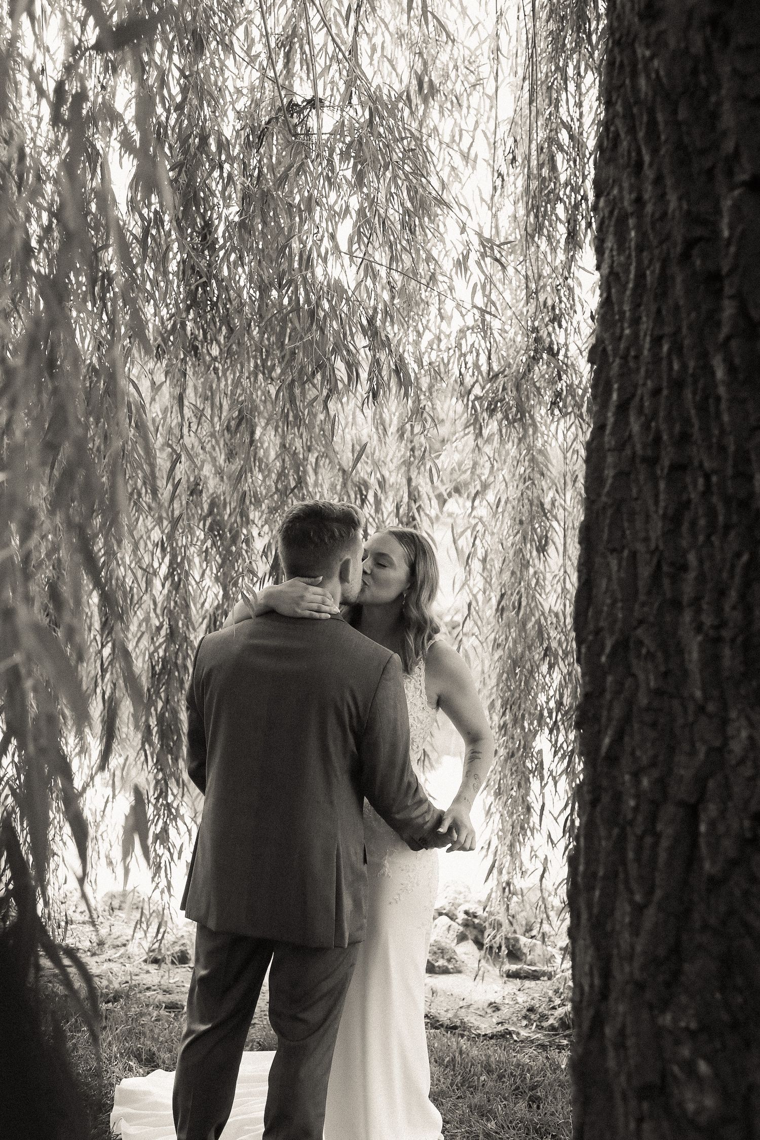 An intimate wedding moment captured under the cascading branches of a willow tree.