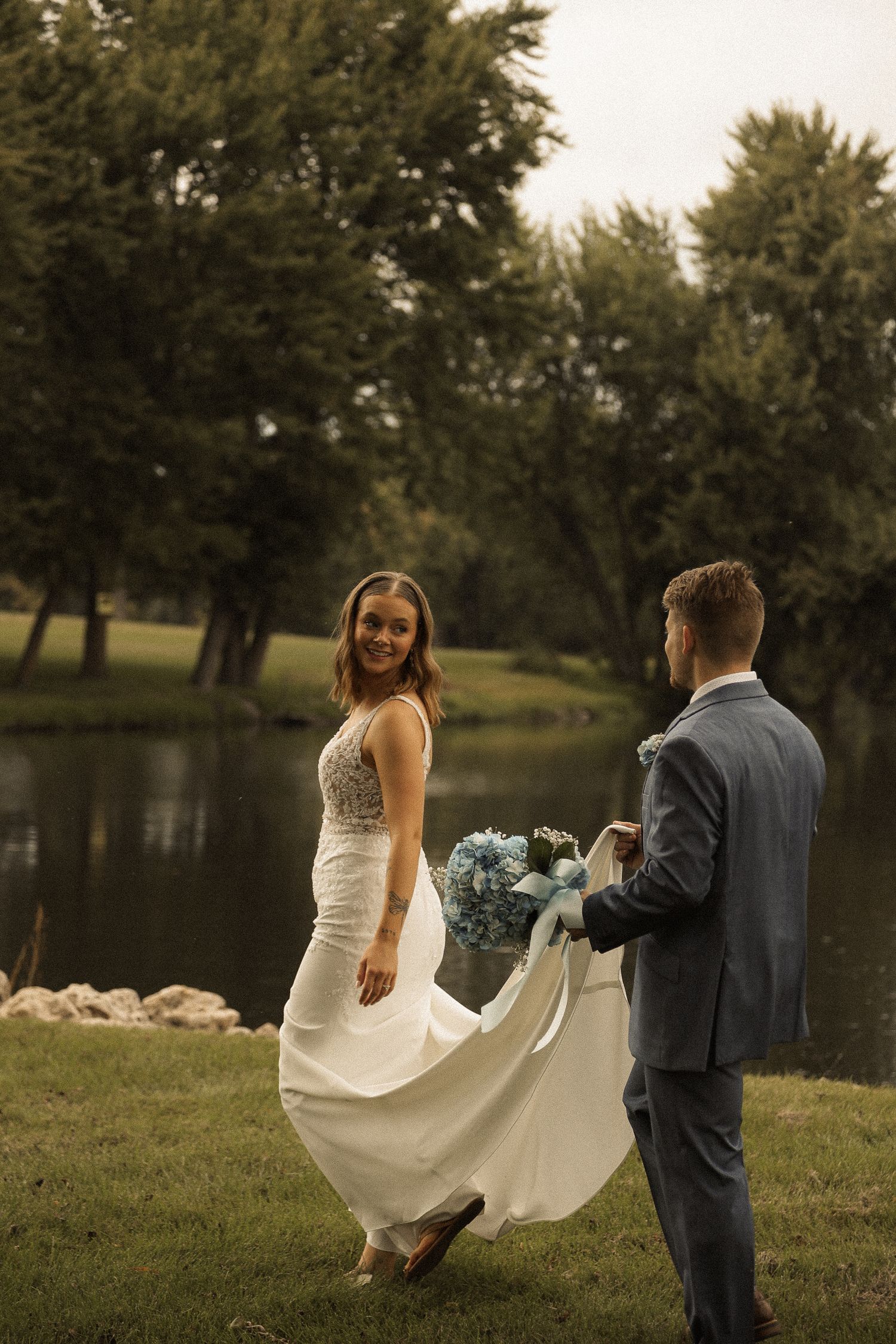 A playful wedding portrait by a pond with flowing white dress and bouquet.
