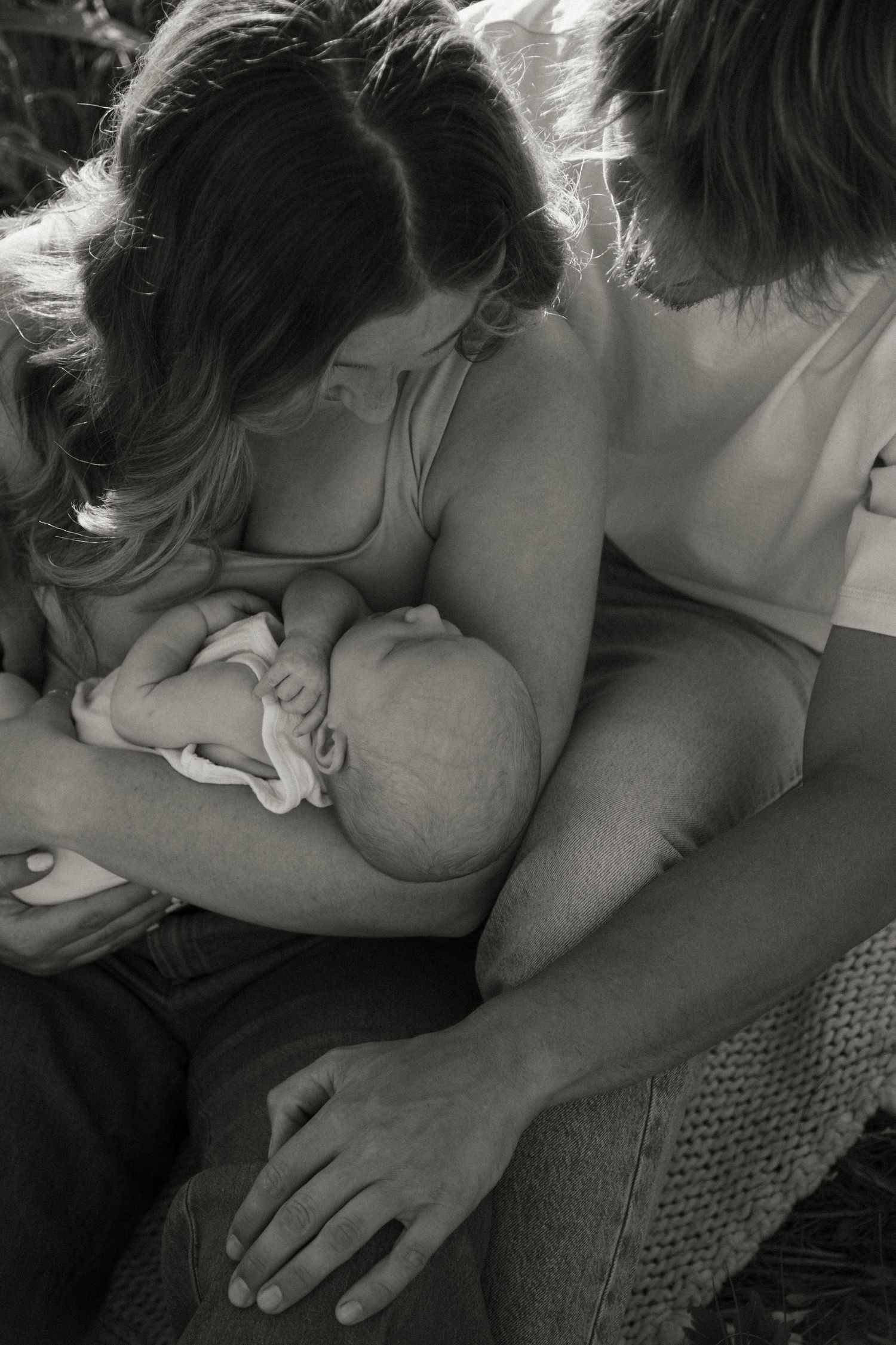 Black and white photo of a mother breastfeeding her newborn baby while family members gather closely around her.