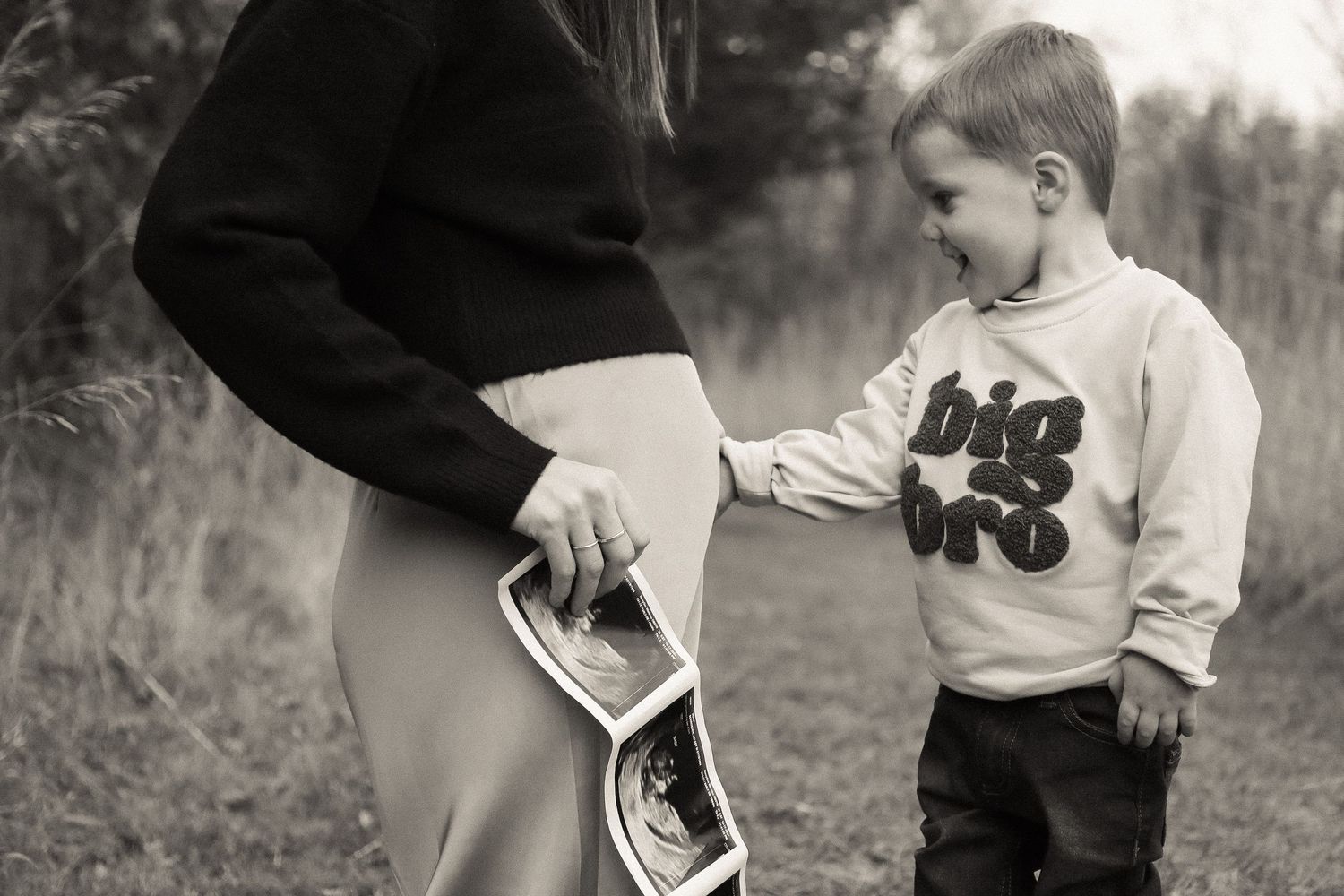A black and white photo of a child looking at ultrasound images outdoors.