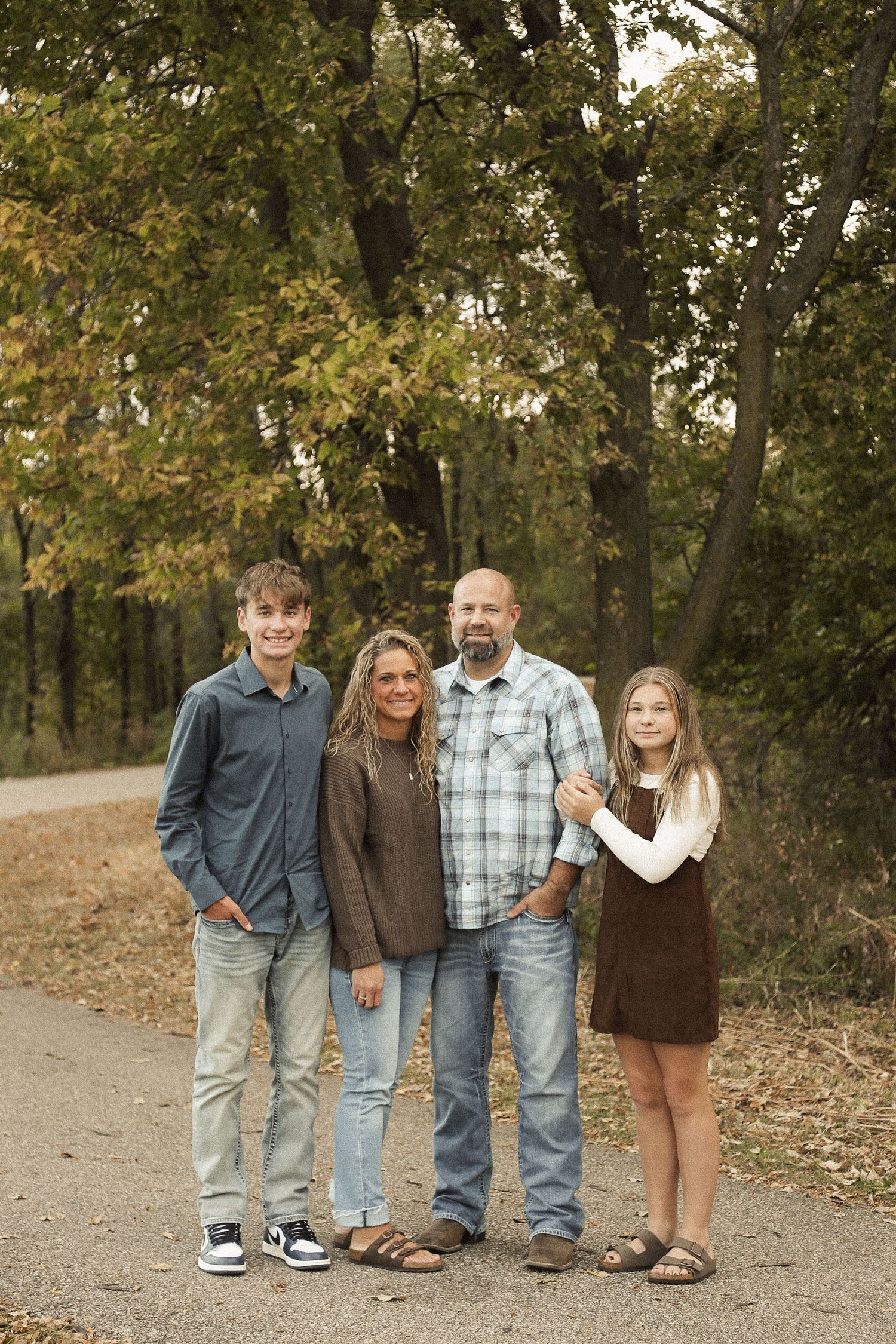 A family stands together on a leaf-covered path in casual autumn attire.
