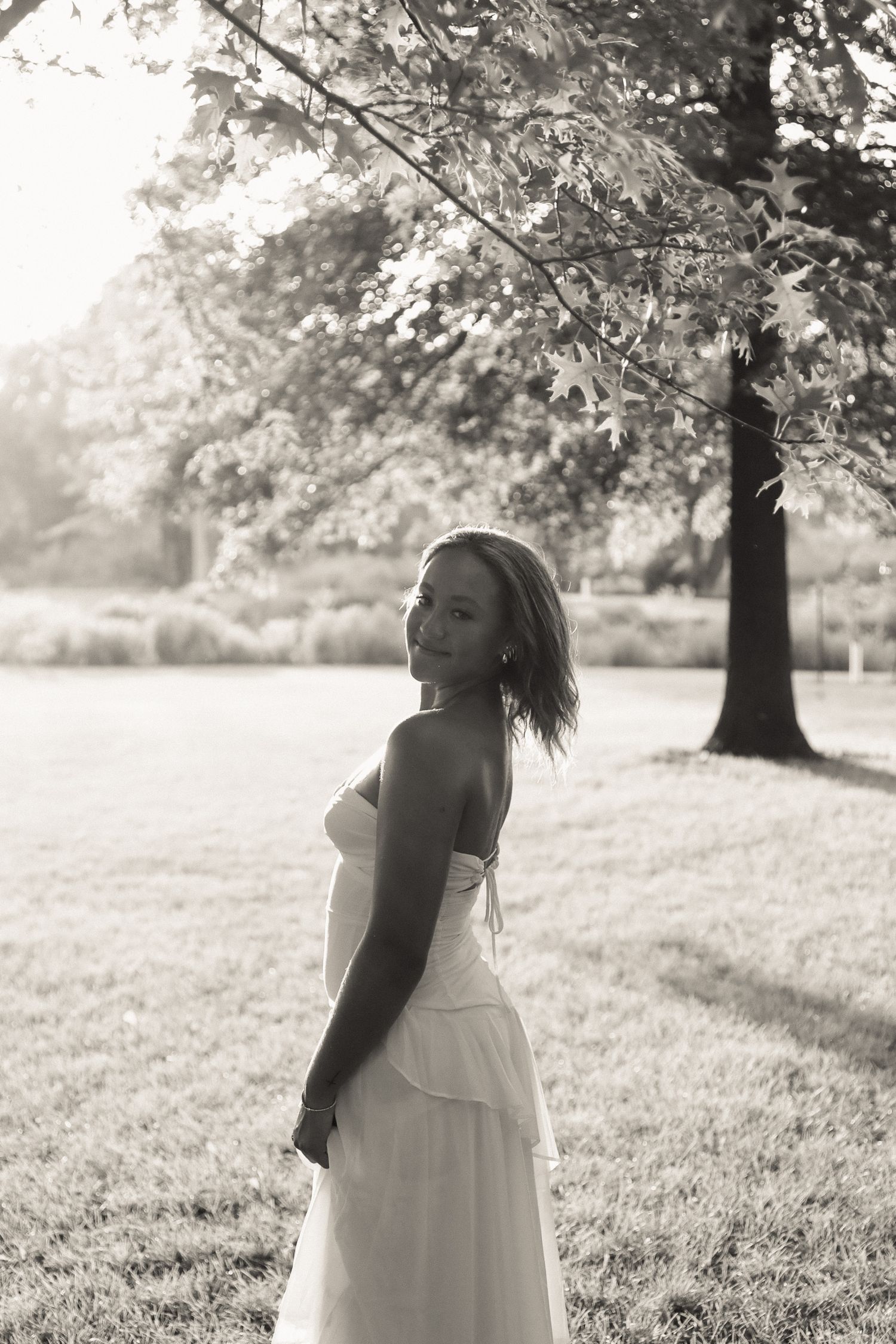 Black and white portrait in a sunlit meadow with trees creating natural framing.