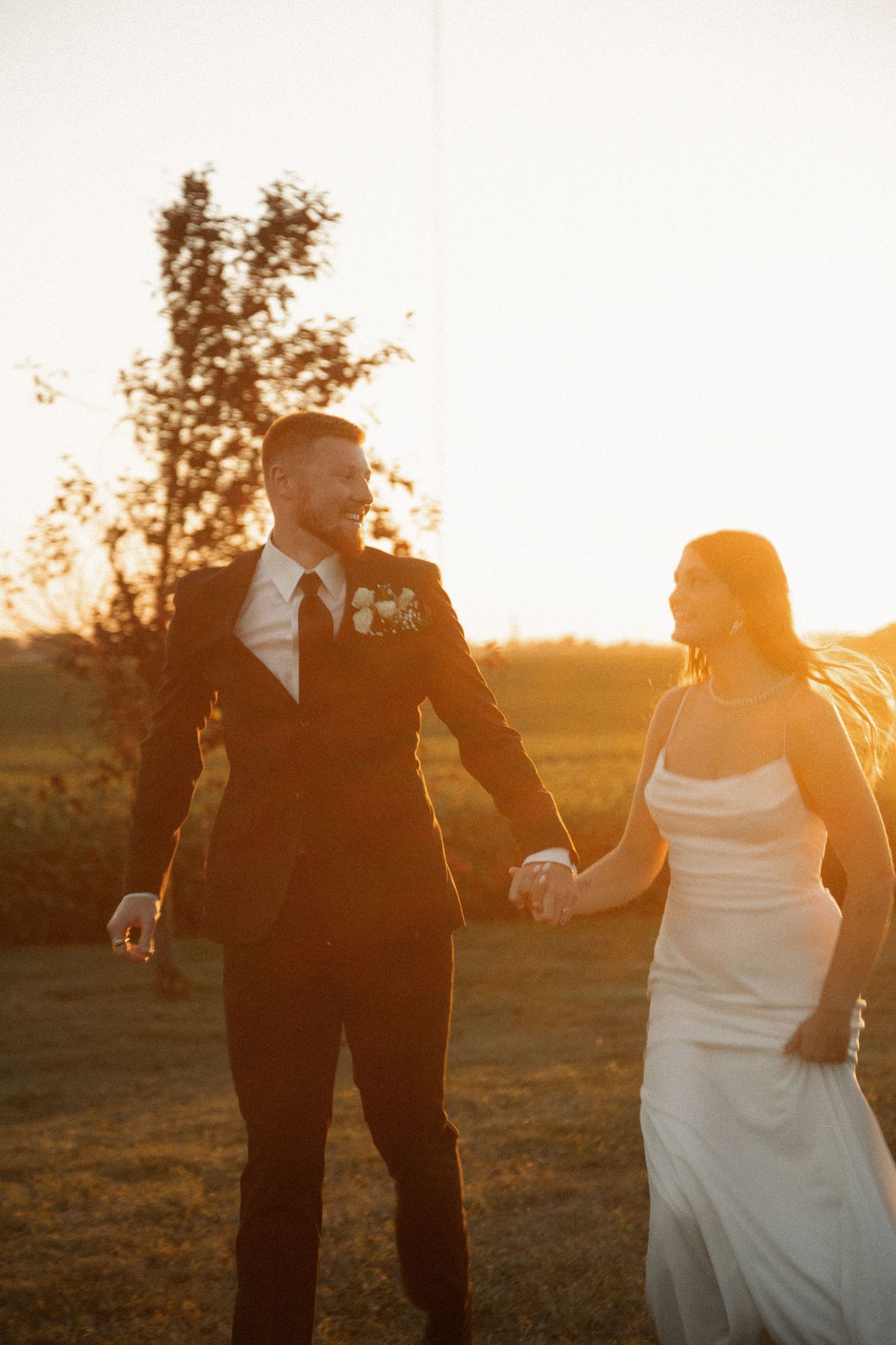 A couple shares a romantic moment at sunset in a field with golden light illuminating their wedding attire.