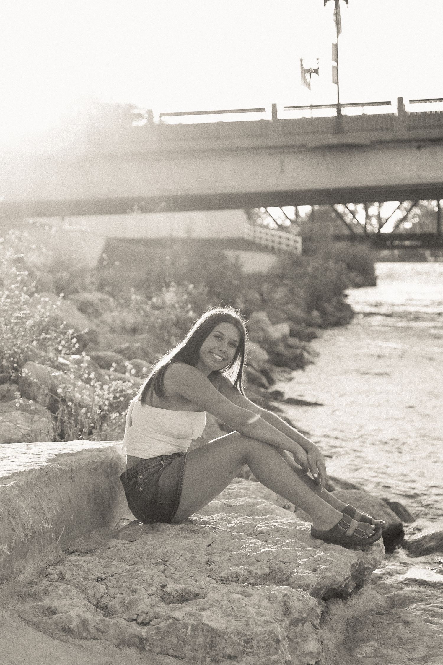 Black and white artistic portraits taken on rocky riverbank with bridge in background.