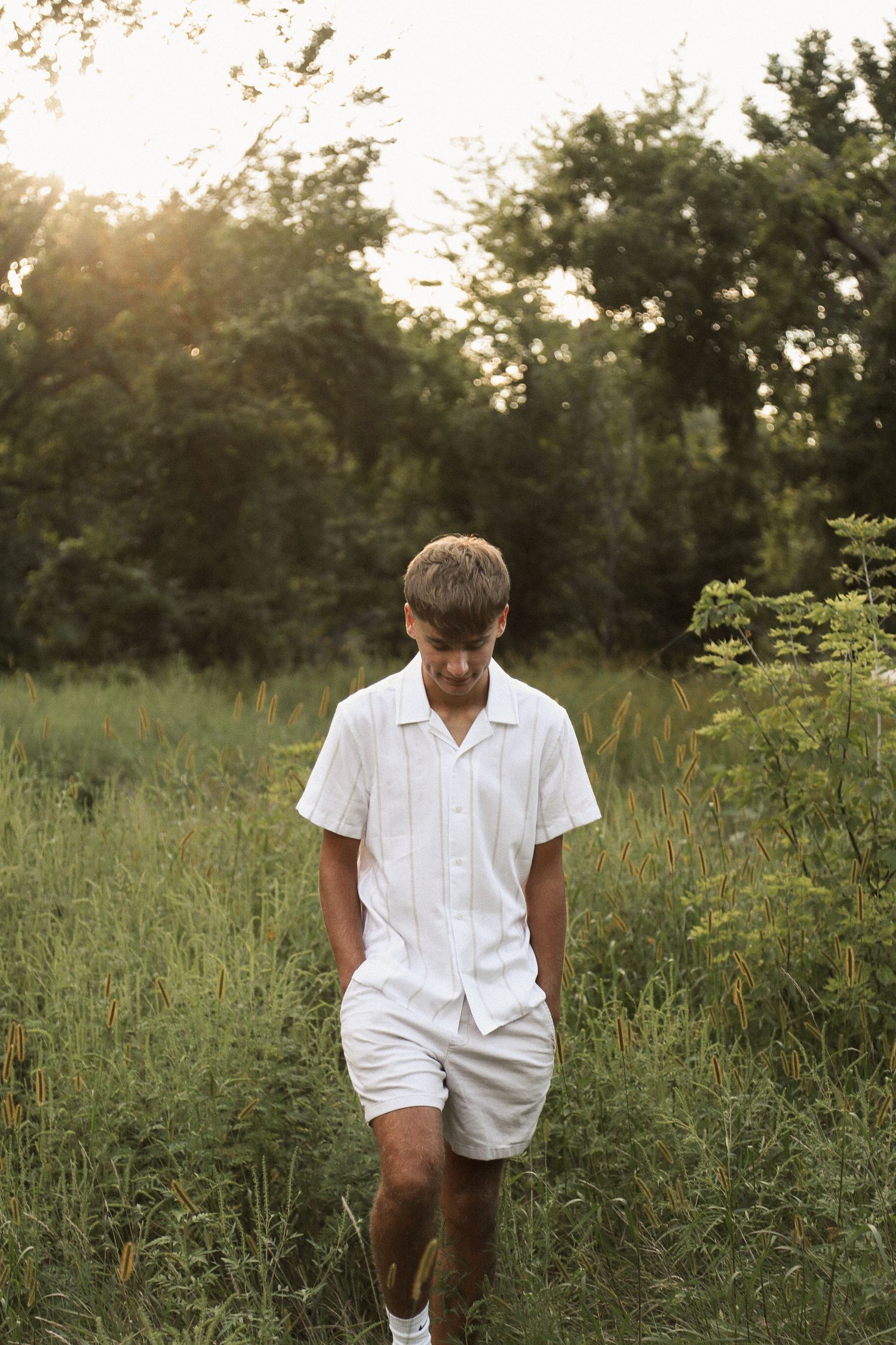 Person wearing white summer clothing poses in wild meadow at golden hour.