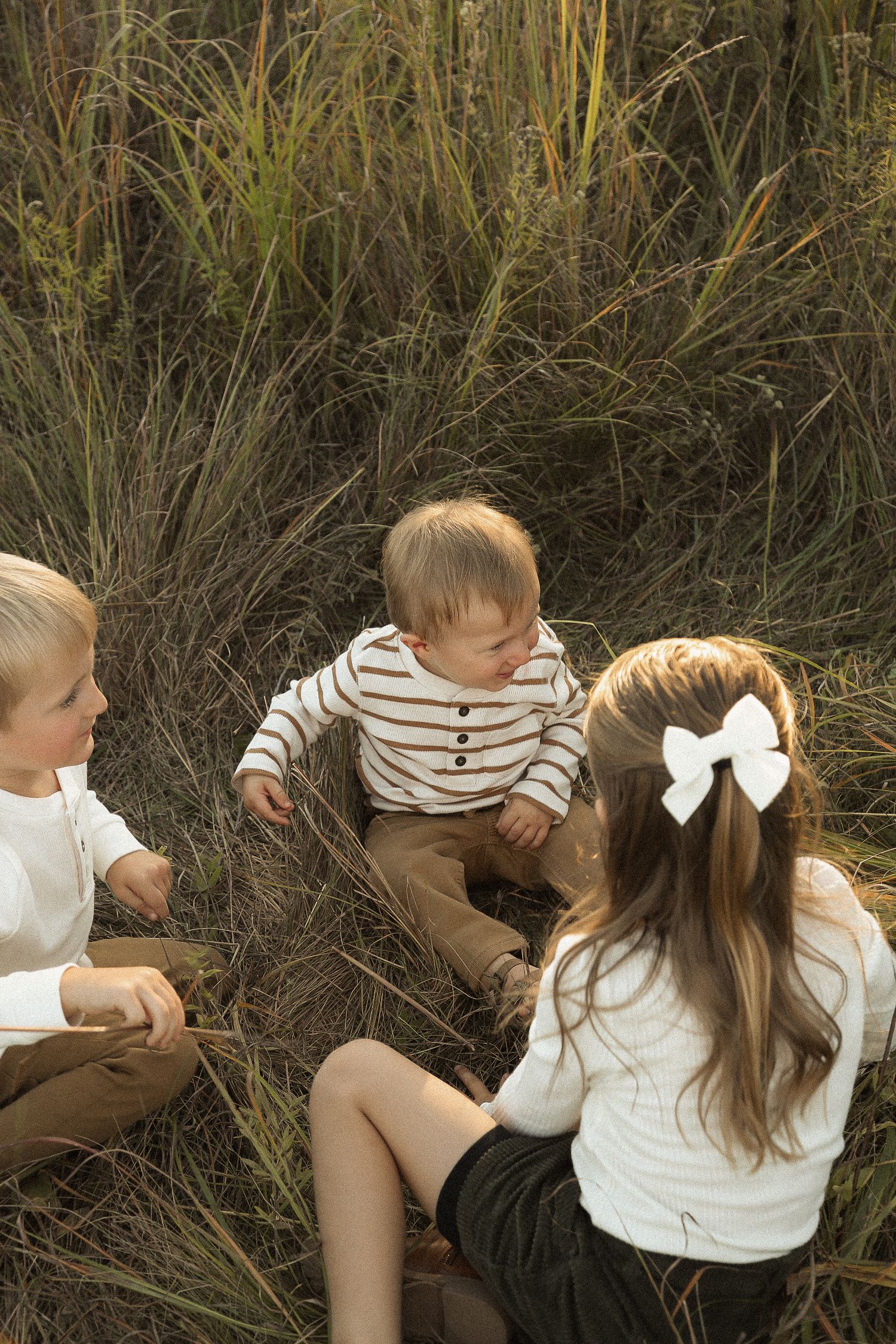 Children playing together in tall grass during a golden hour photoshoot.