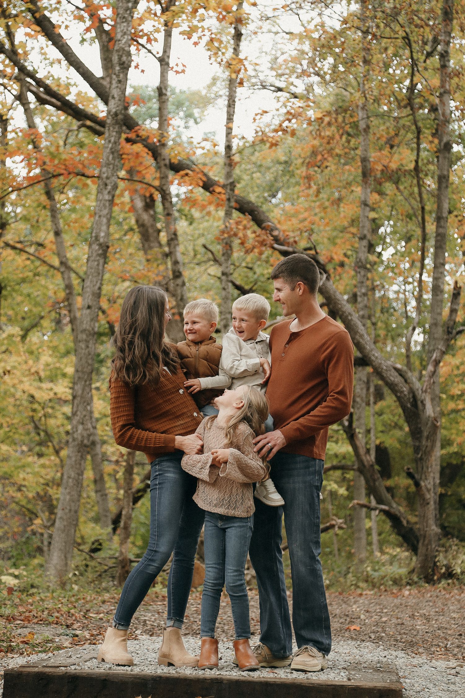A family shares playful moments together in an autumn forest setting with fallen leaves and trees.