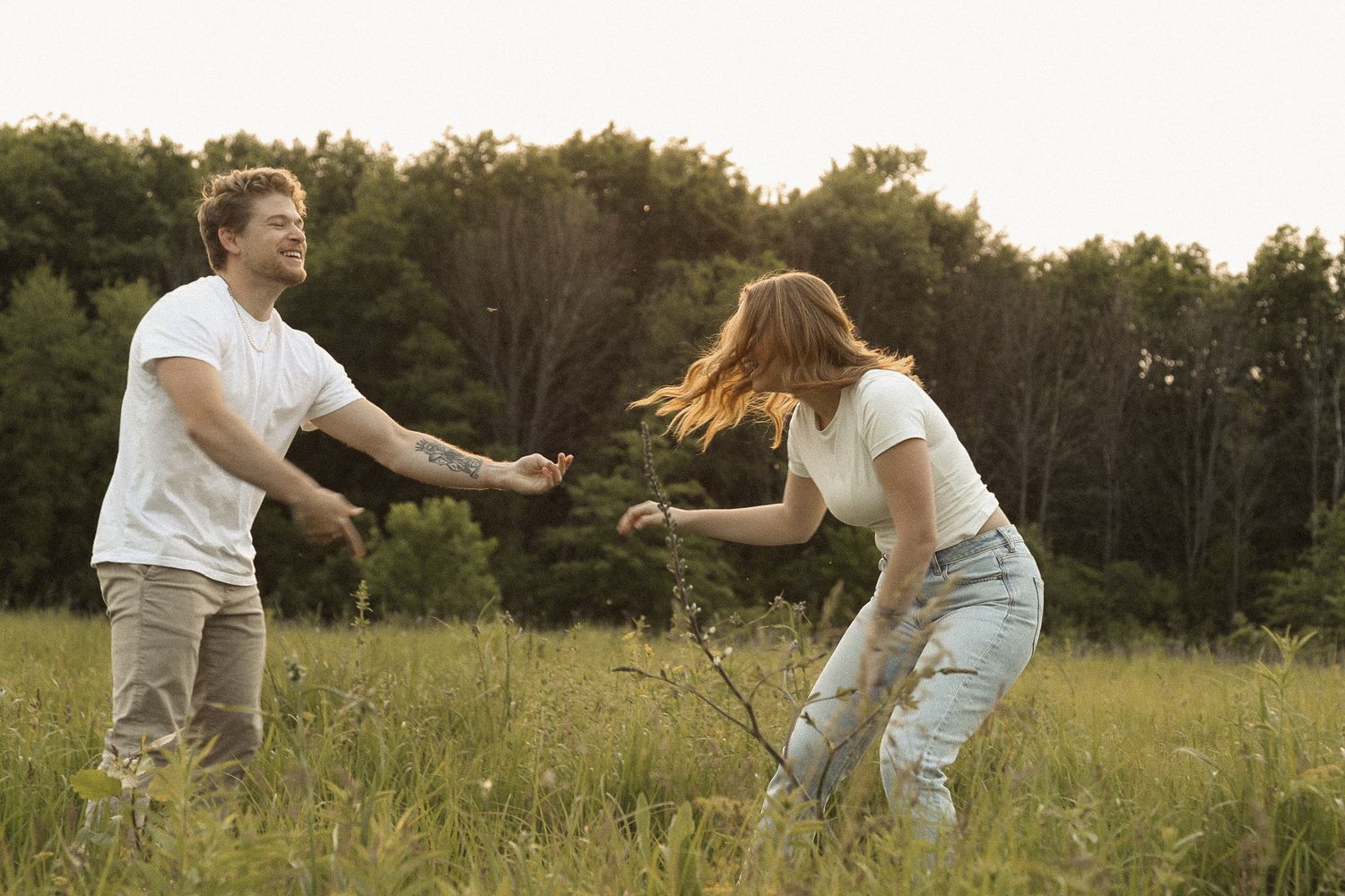 Two people playing and spinning in a grassy field at sunset.