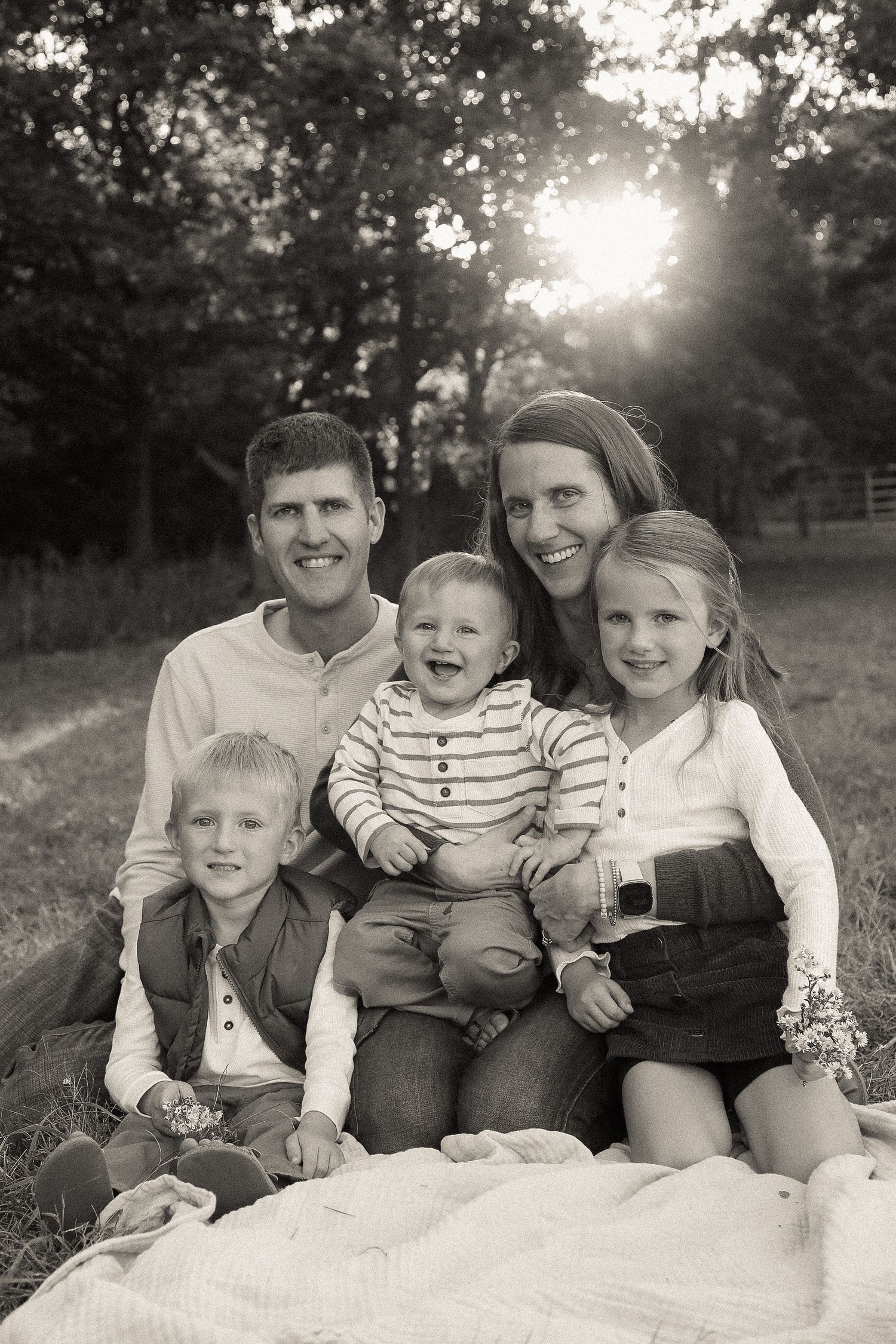 A family group poses together on a white blanket during an outdoor photo session.