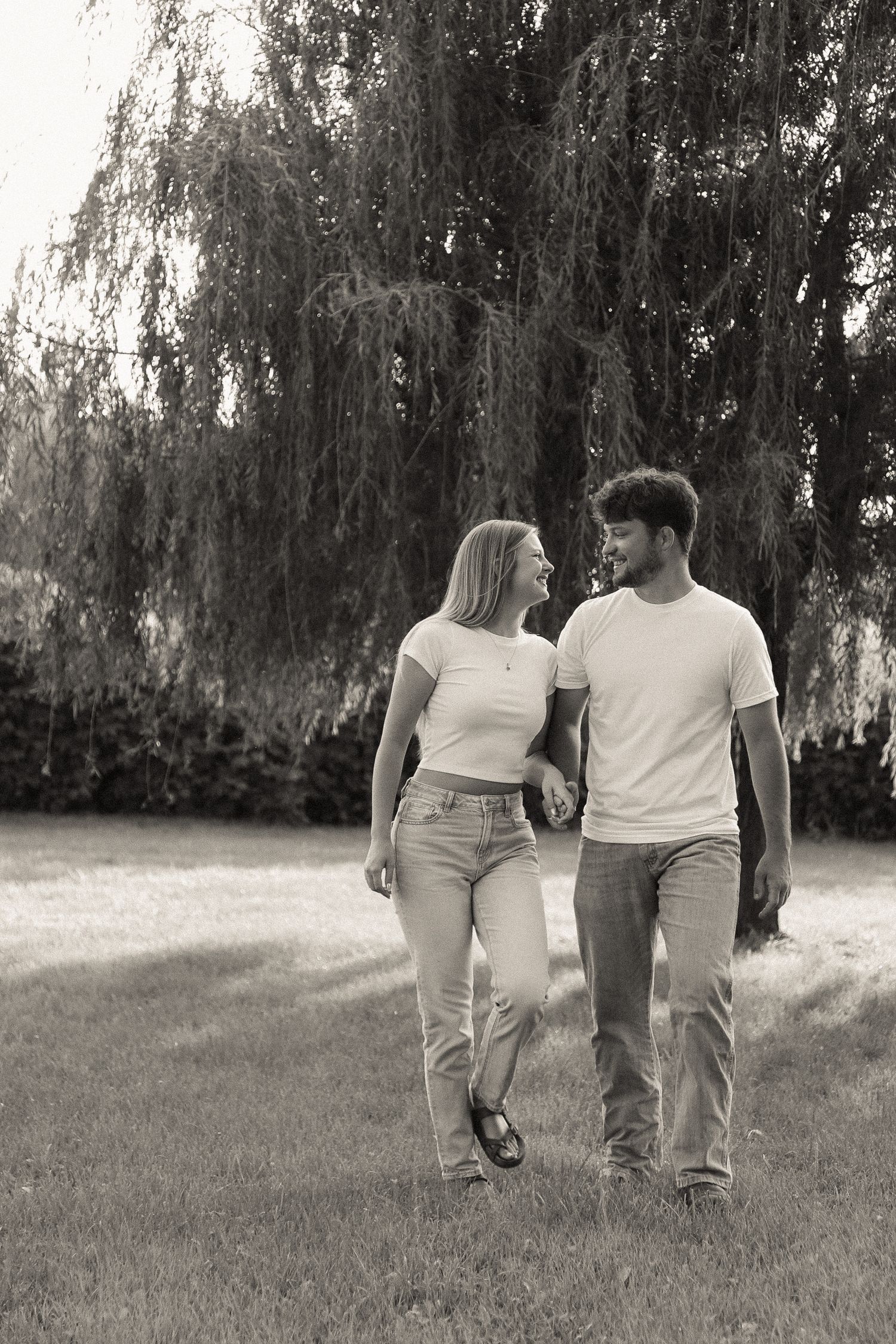 Couple in white shirts and jeans walking together through a park.