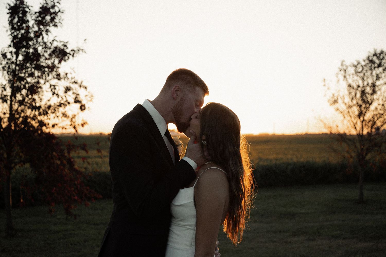 Couple sharing intimate moment at sunset with golden light illuminating their silhouettes.