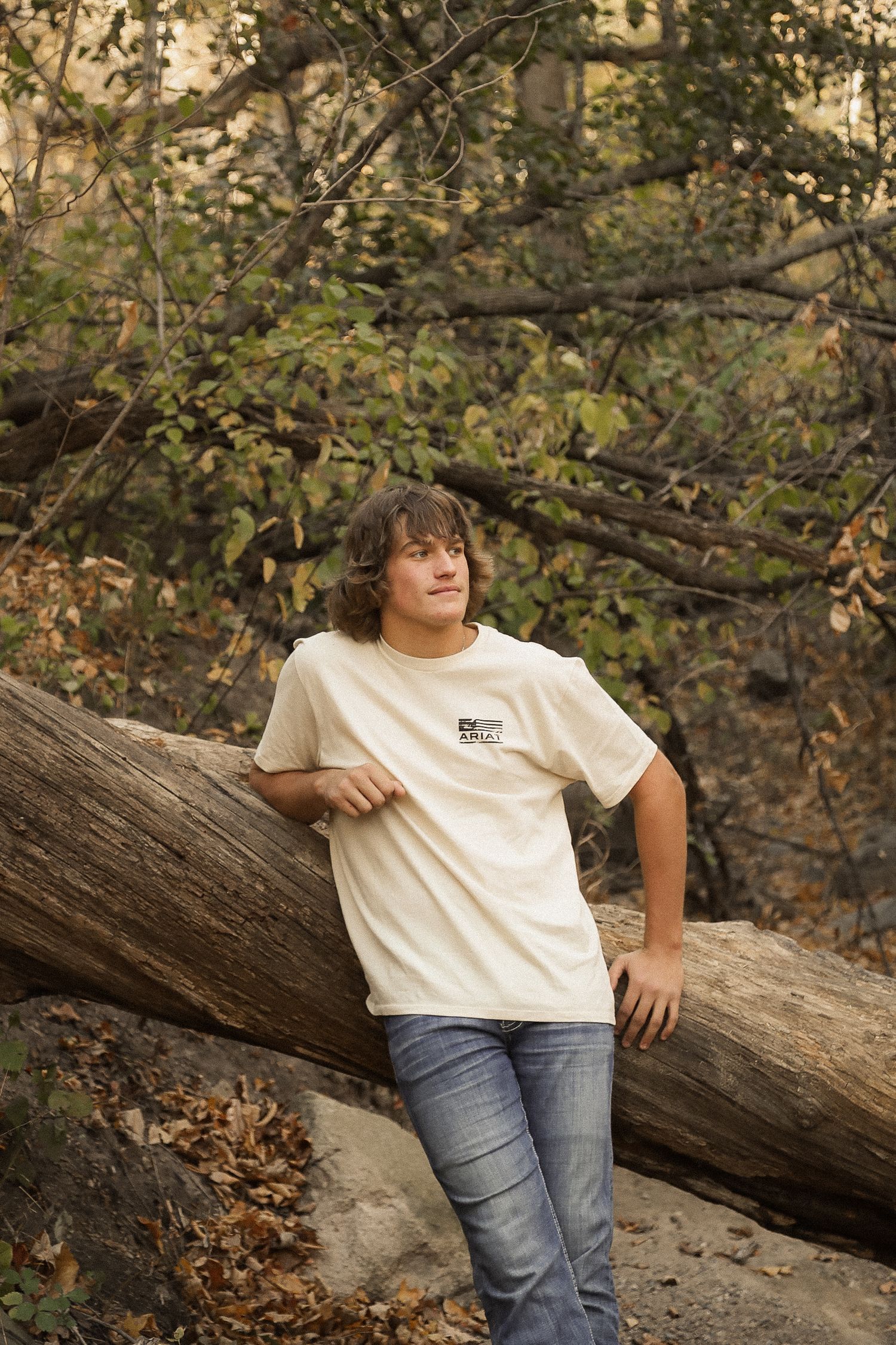 Casual portrait on fallen log in wooded area wearing white t-shirt and jeans.