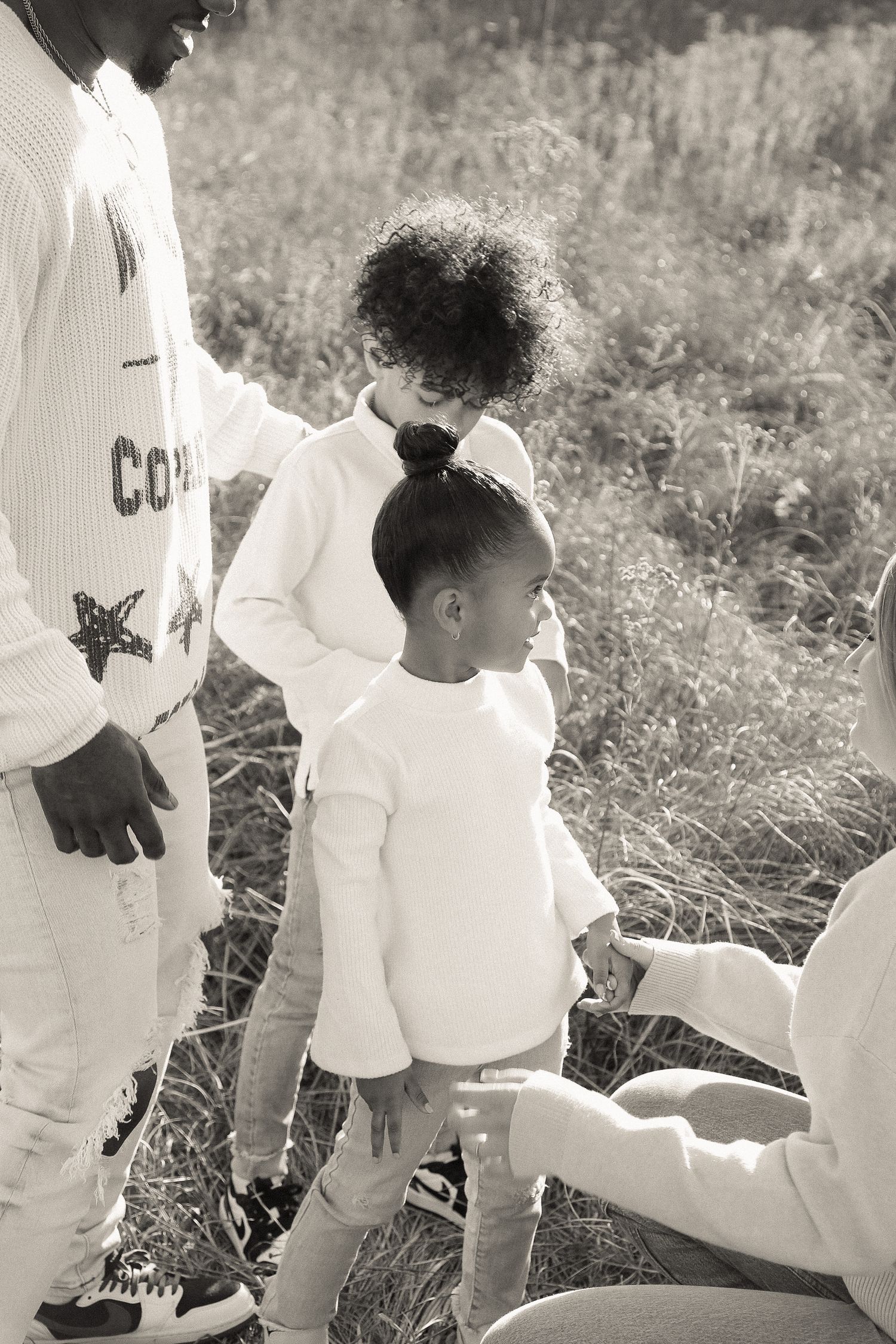Two children in white sweaters stand close together during an outdoor family photoshoot.